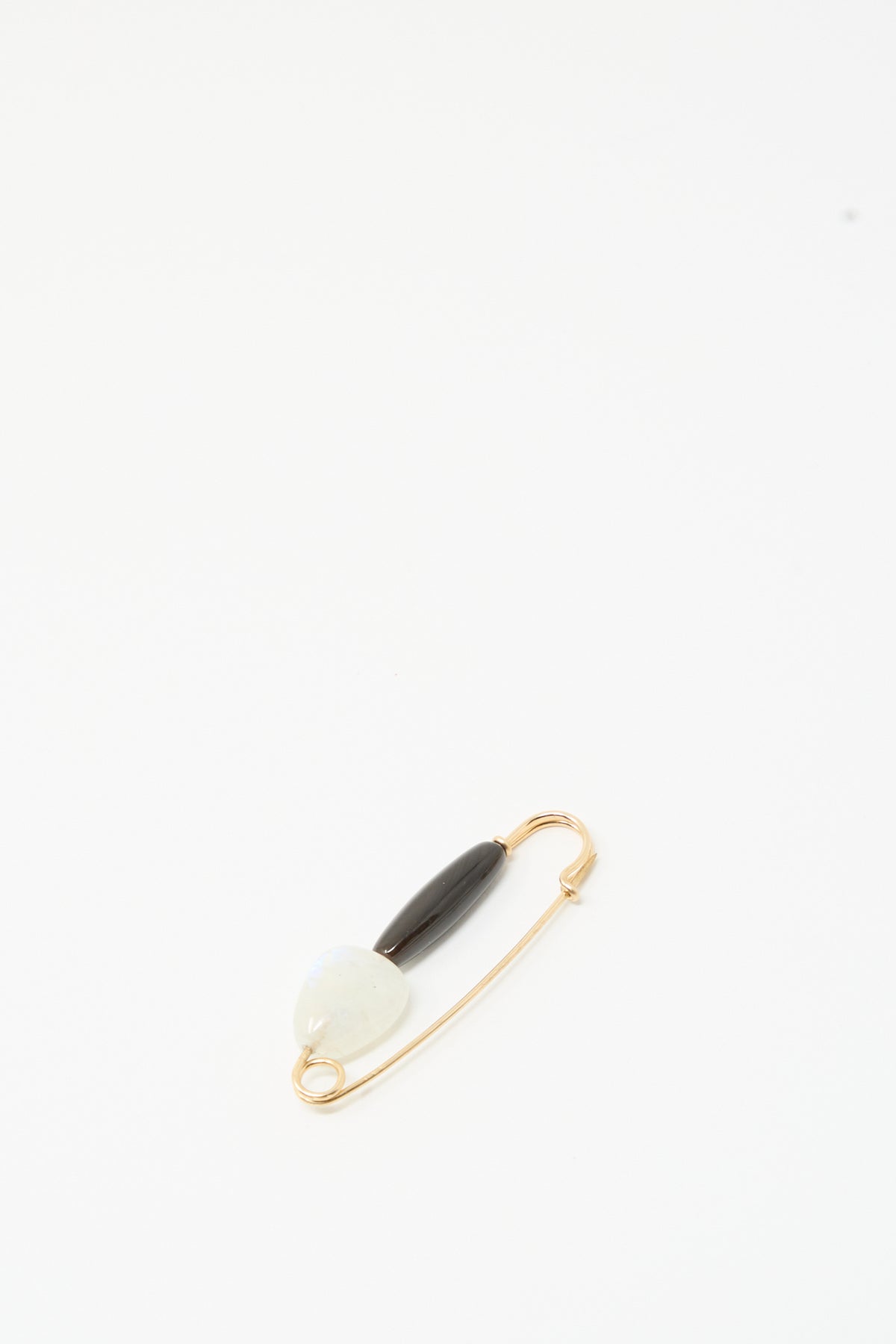 The Moonstone and Agate Pin by Mary MacGill features a gold-filled wire with a white bead and black agate, displayed on a plain white background.