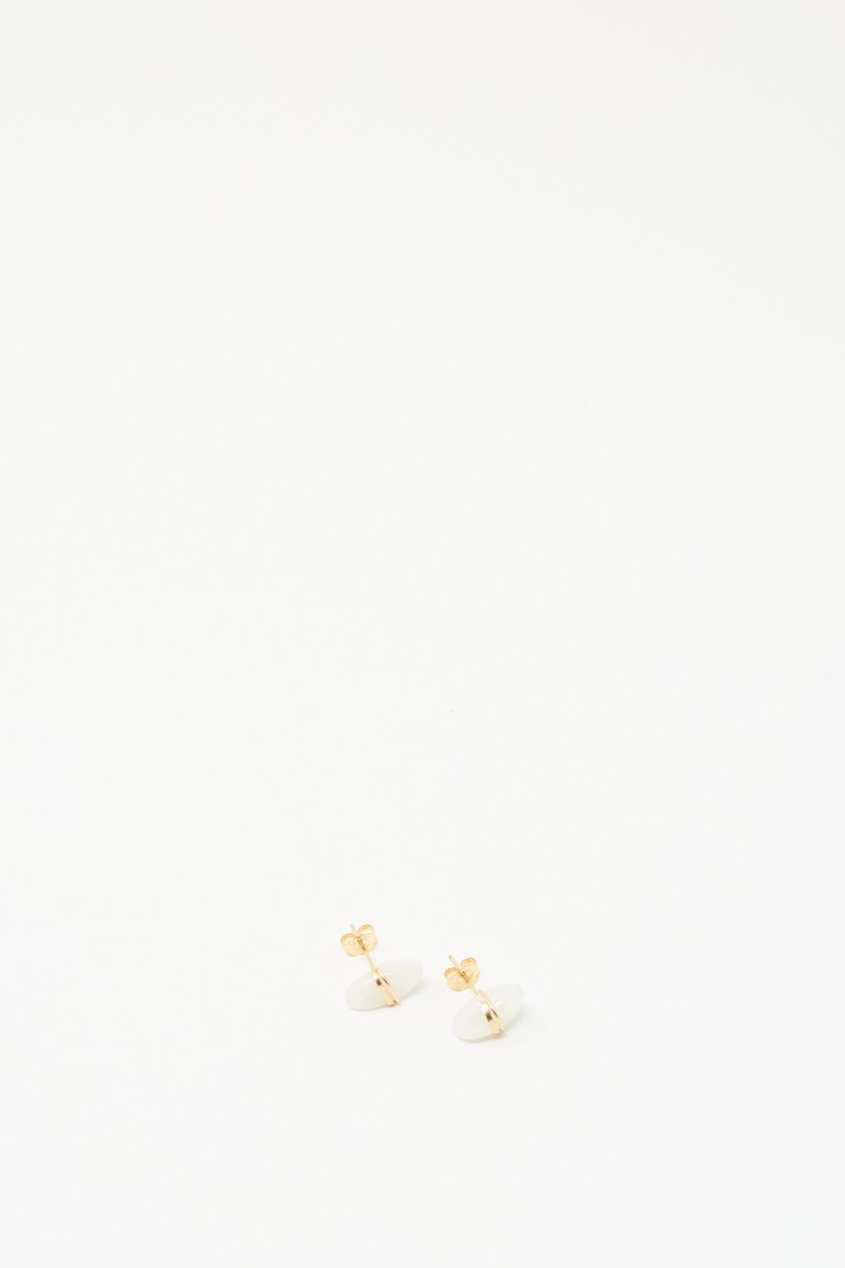 A pair of small gold stud earrings with white oval moonstones, photographed on a seamless white background.