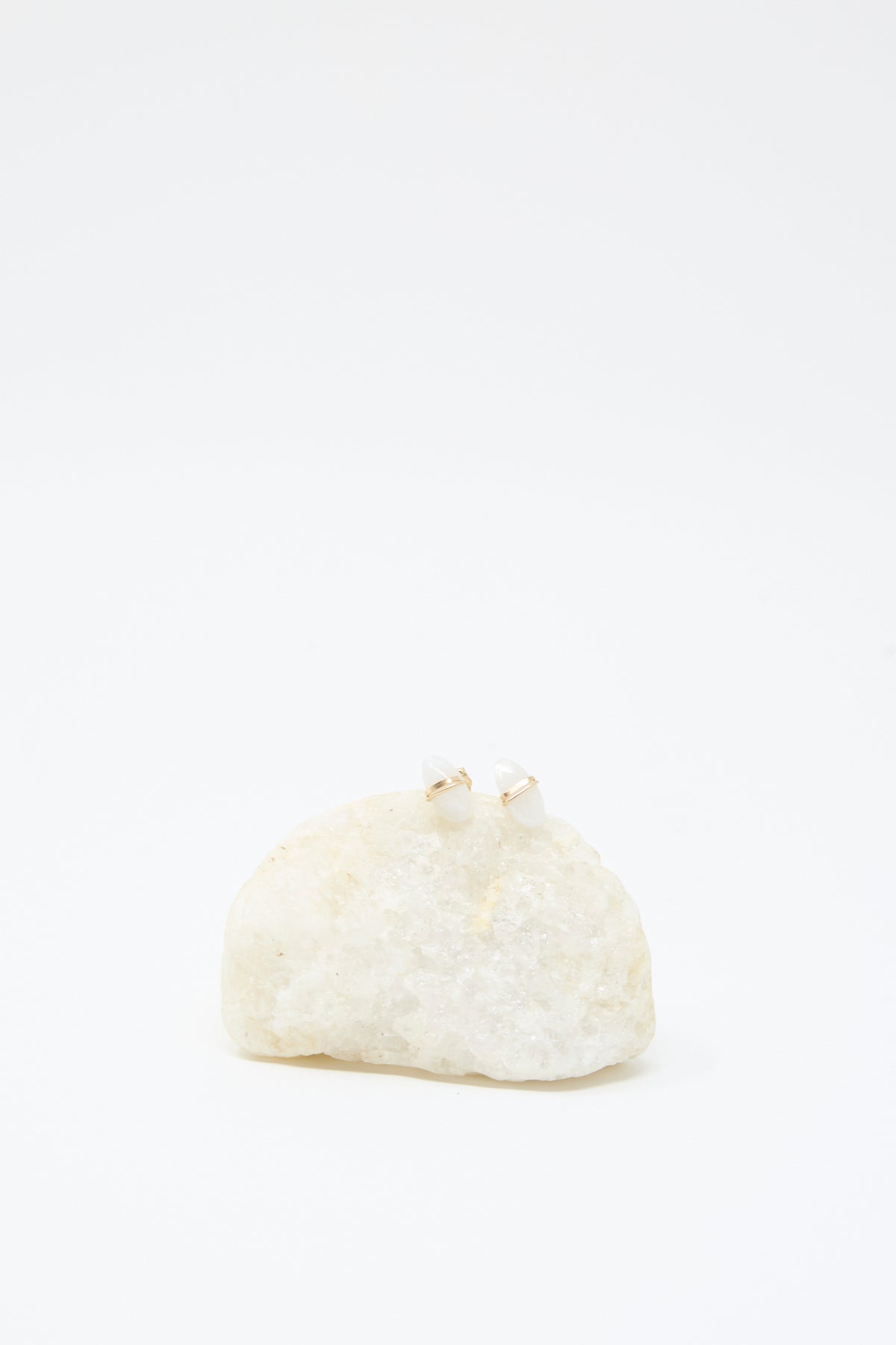 Moonstone Studs by Mary MacGill are displayed on a rough white stone, their gold and white design standing out elegantly against a plain white background.