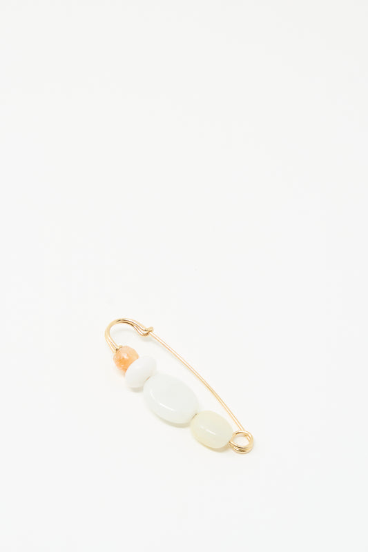 The Newsprint Pin by Mary MacGill is a handmade gold safety pin with three white beads and one peach bead, displayed on a plain white background.