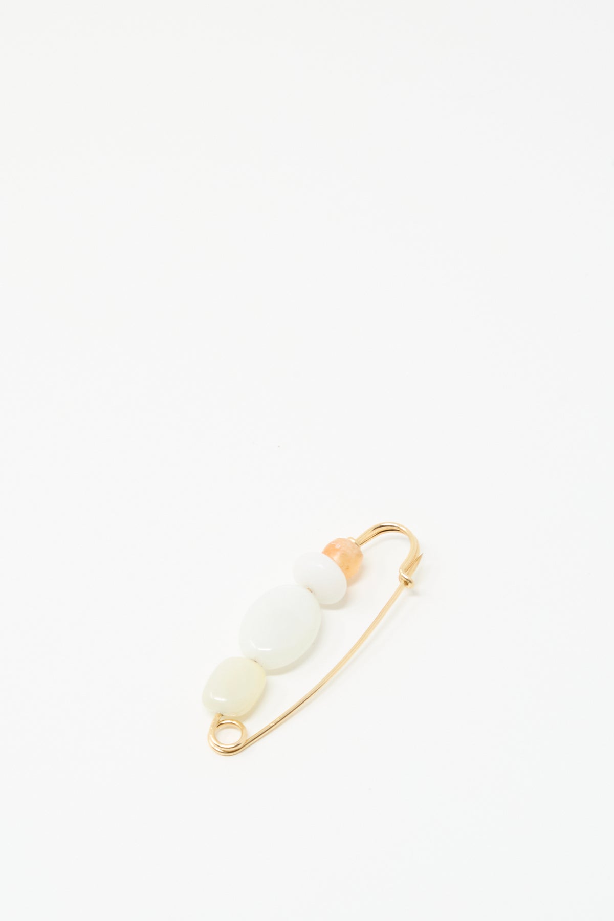 The Newsprint Pin by Mary MacGill is a handmade gold safety pin with three white beads and one peach bead, displayed on a plain white background.