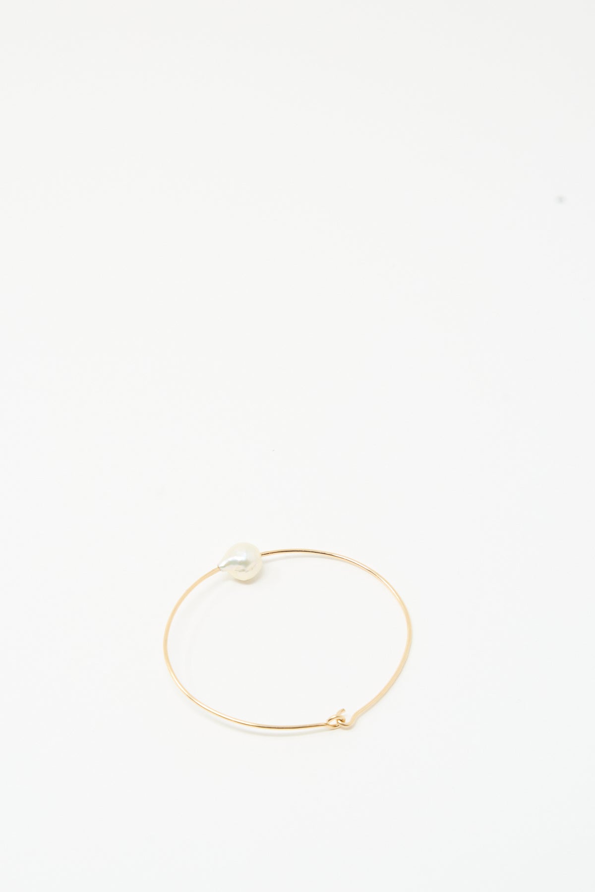The Mary MacGill Petite Baroque Pearl Cuff in White, a slim gold-filled bracelet with a white pearl, rests on a simple white background.