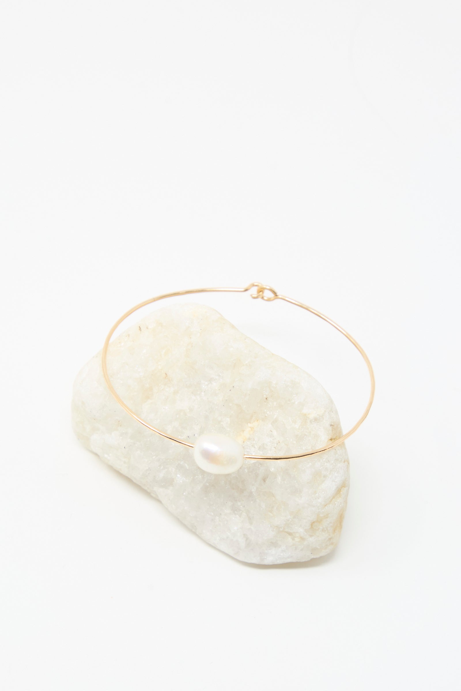 The Mary MacGill Petite Baroque Pearl Cuff in White, a delicate gold-filled bracelet featuring a single white pearl, is displayed on a white stone with a white background.