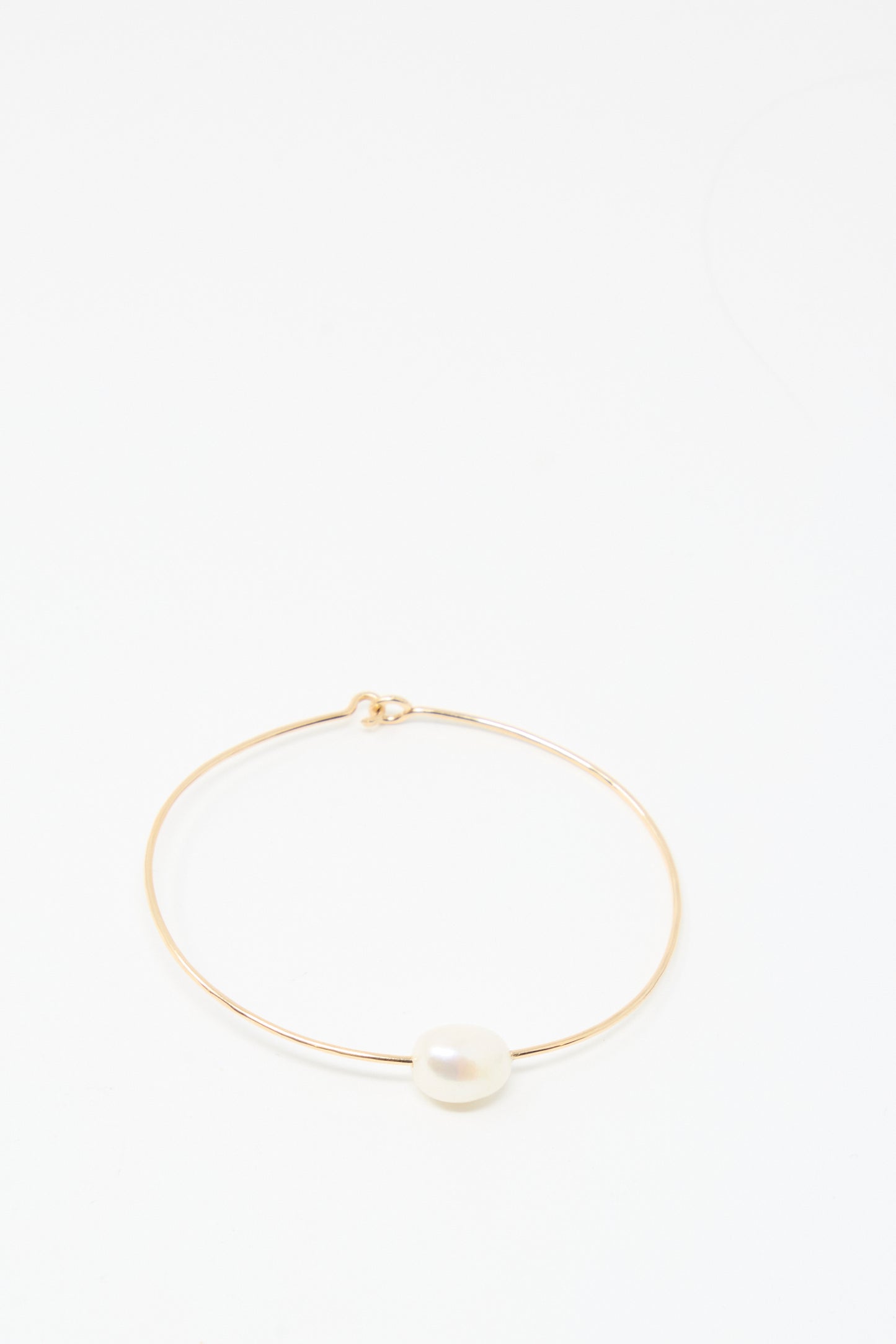 The Mary MacGill Petite Baroque Pearl Cuff in White is a slim, handmade gold-filled bracelet featuring a single white pearl at its center, elegantly displayed on a plain white background.