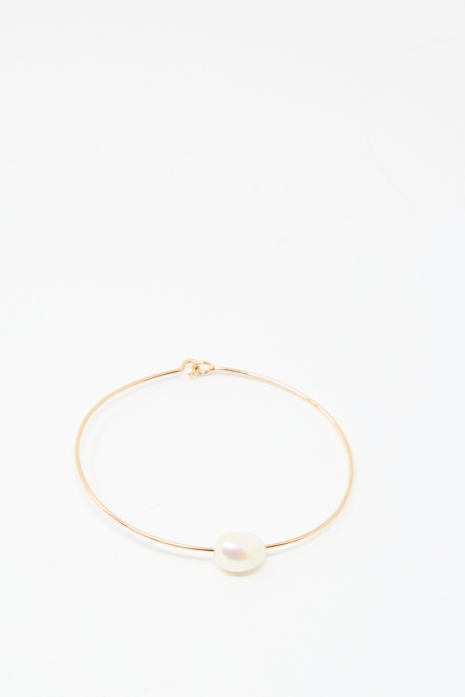 The Mary MacGill Petite Baroque Pearl Cuff in White is a slim, handmade gold-filled bracelet featuring a single white pearl at its center, elegantly displayed on a plain white background.