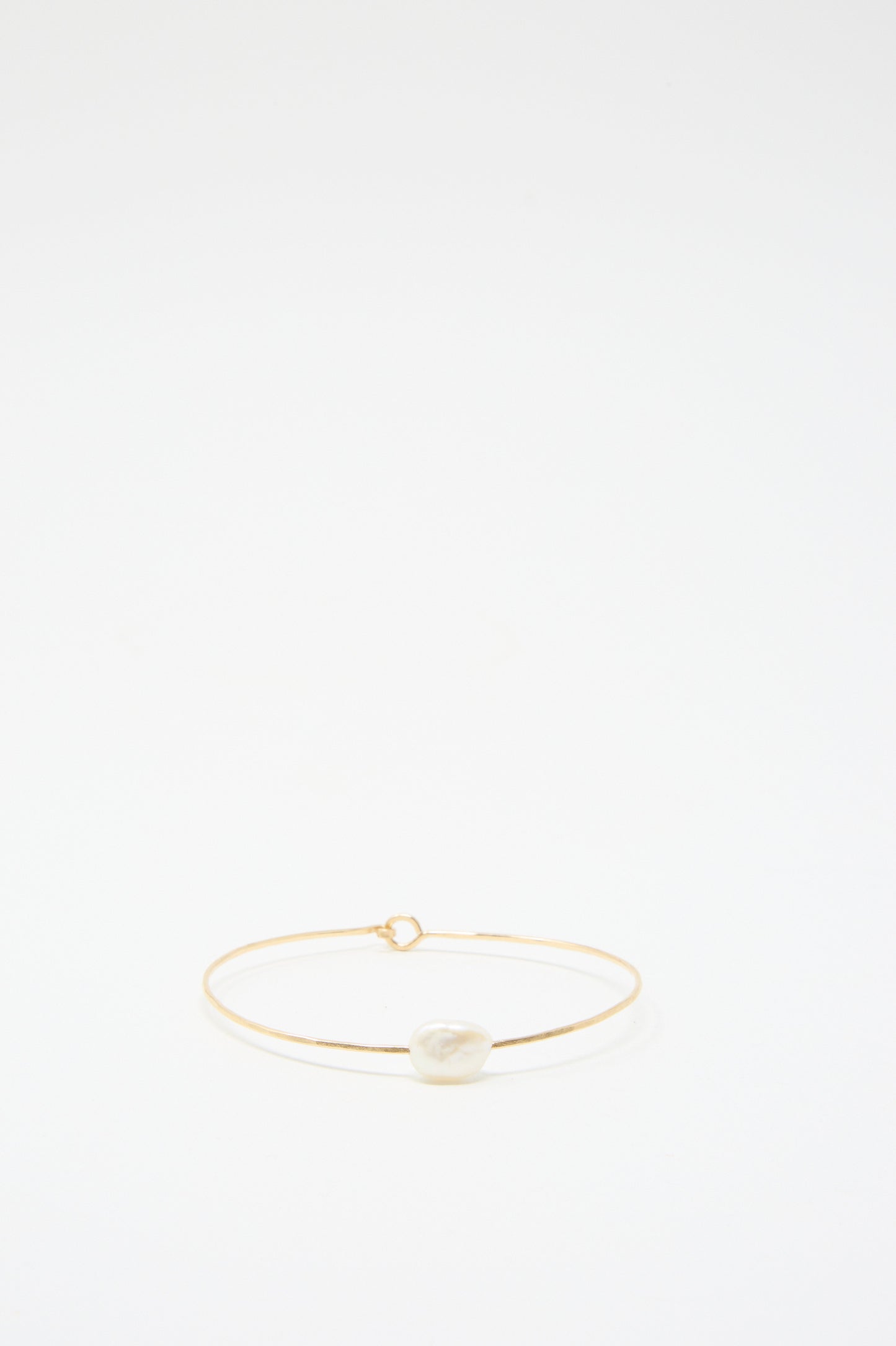 Set against a plain white background, the Petite Baroque Pearl Cuff Bracelet in White by Mary MacGill showcases a single irregular white stone, delicately crafted with gold-filled wire.