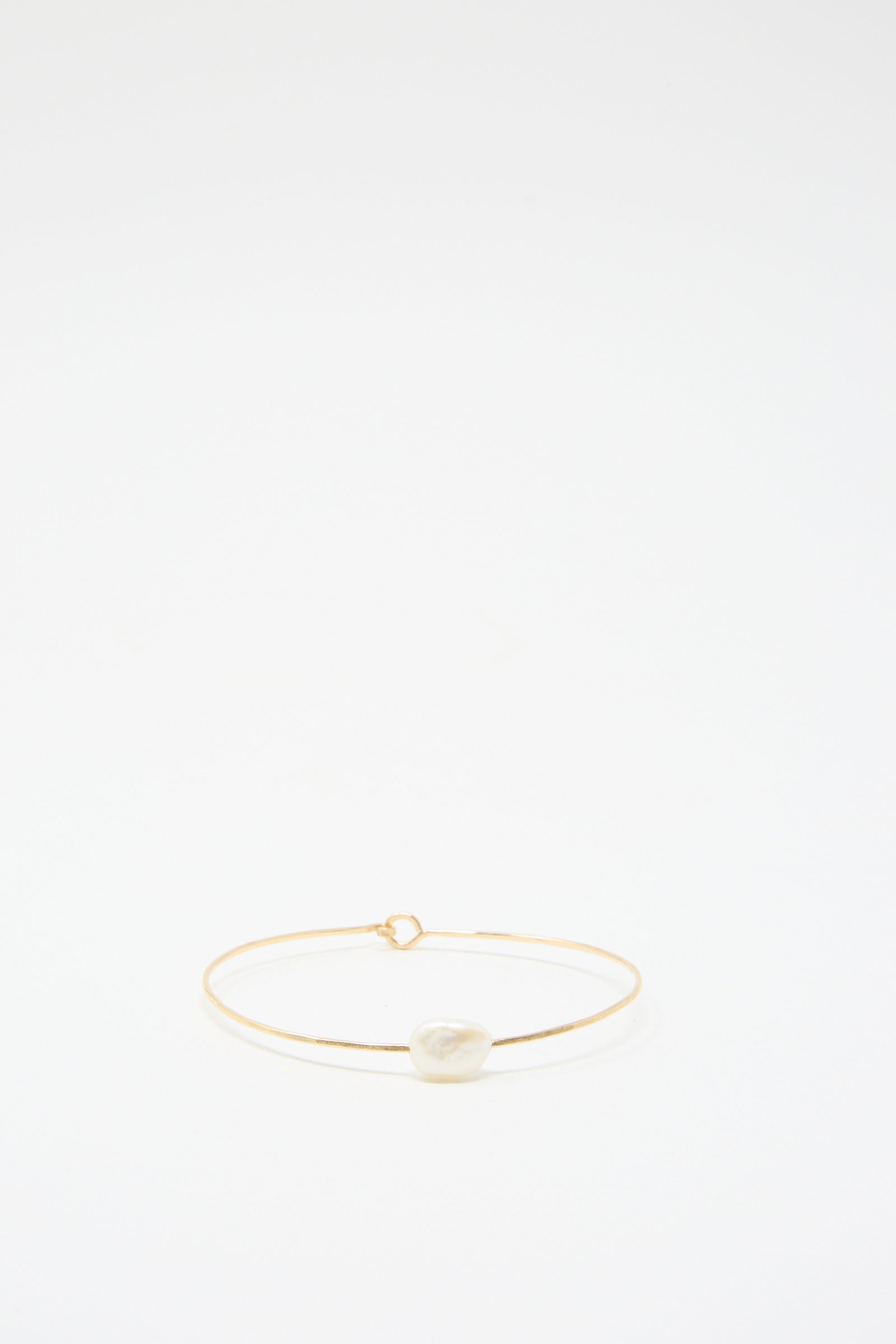 Set against a plain white background, the Petite Baroque Pearl Cuff Bracelet in White by Mary MacGill showcases a single irregular white stone, delicately crafted with gold-filled wire.