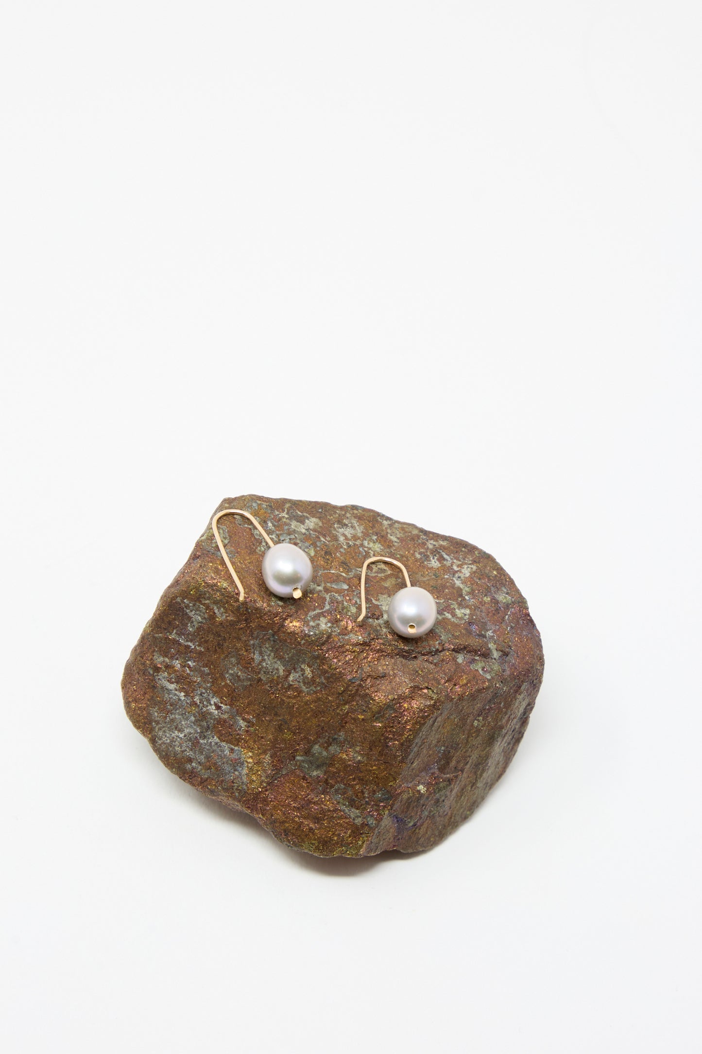 Petite Baroque Pearl Drop Earrings in Silver by Mary MacGill, featuring handmade Hudson Valley artistry, displayed on a rough brown rock with a plain white background.