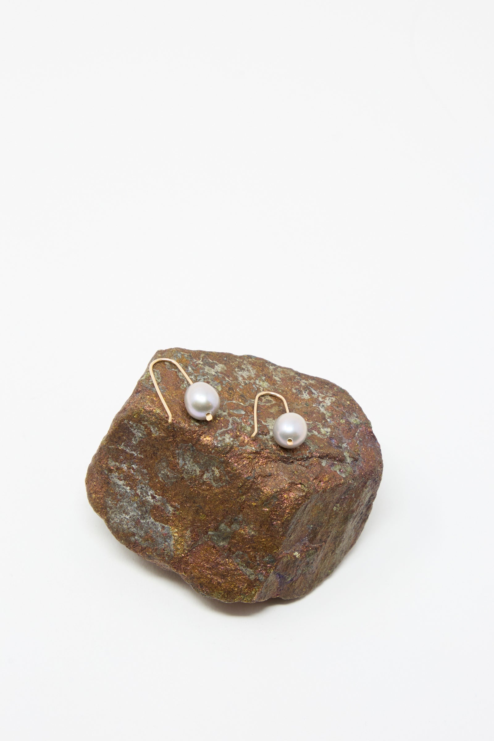 Petite Baroque Pearl Drop Earrings in Silver by Mary MacGill, featuring handmade Hudson Valley artistry, displayed on a rough brown rock with a plain white background.