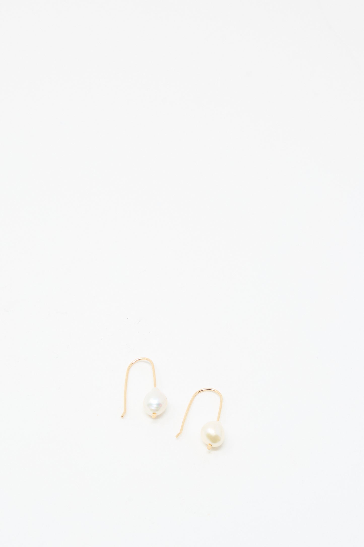 The Petite Baroque Pearl Drop Earrings in White by Mary MacGill feature single white pearls on gold-filled hooks. Displayed on a plain white background, these handmade earrings bring elegance to any look.