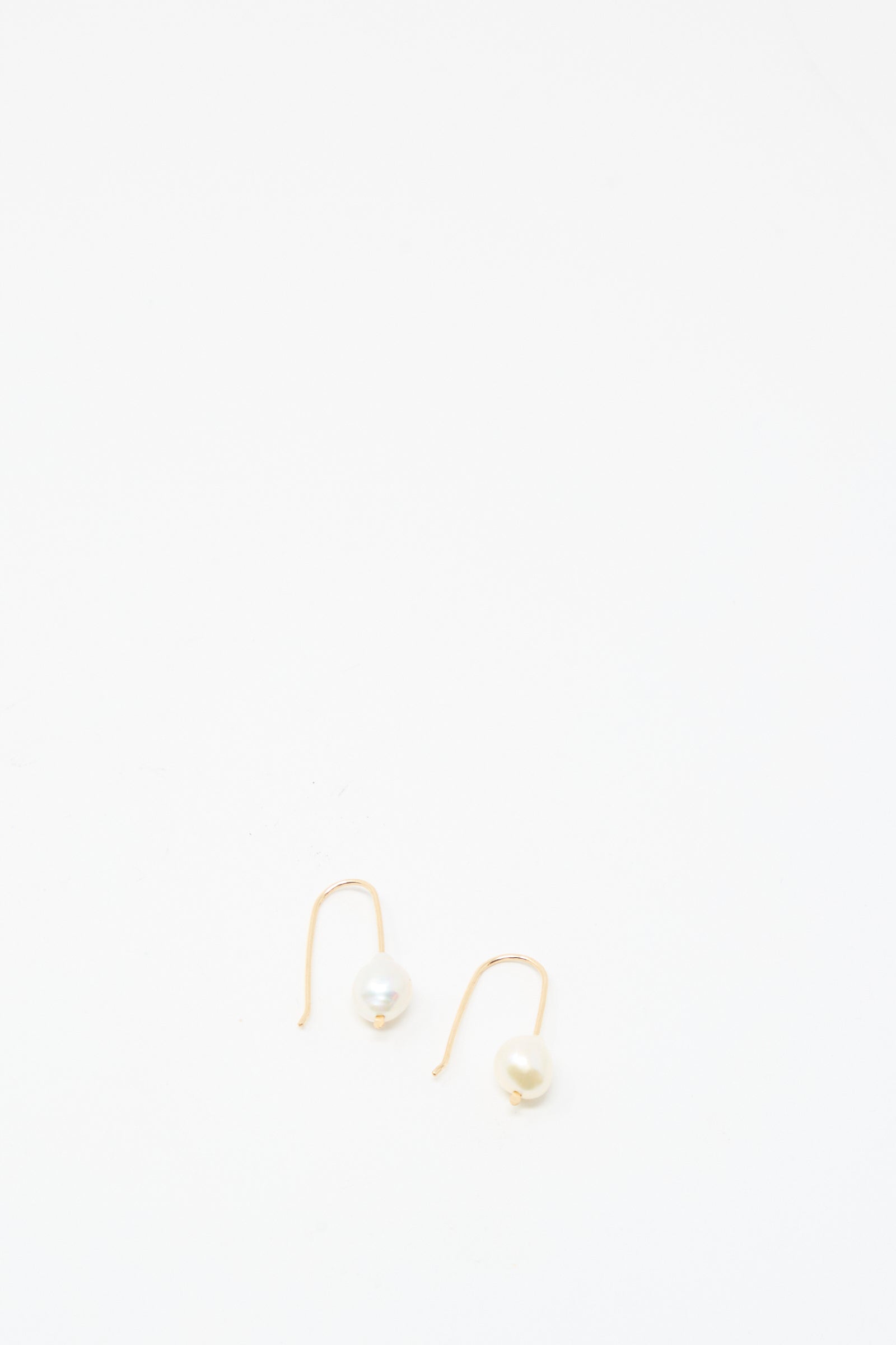 The Petite Baroque Pearl Drop Earrings in White by Mary MacGill feature single white pearls on gold-filled hooks. Displayed on a plain white background, these handmade earrings bring elegance to any look.