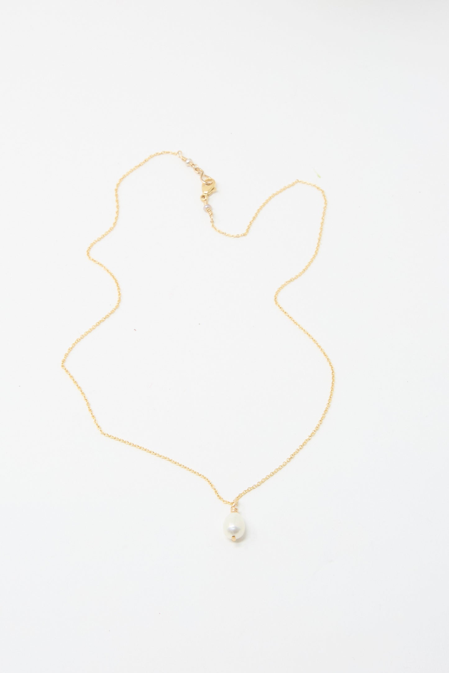 The Mary MacGill Petite Baroque Pearl Drop Necklace in White features a single  pearl pendant gracefully suspended from a gold-filled chain on a pristine white background.