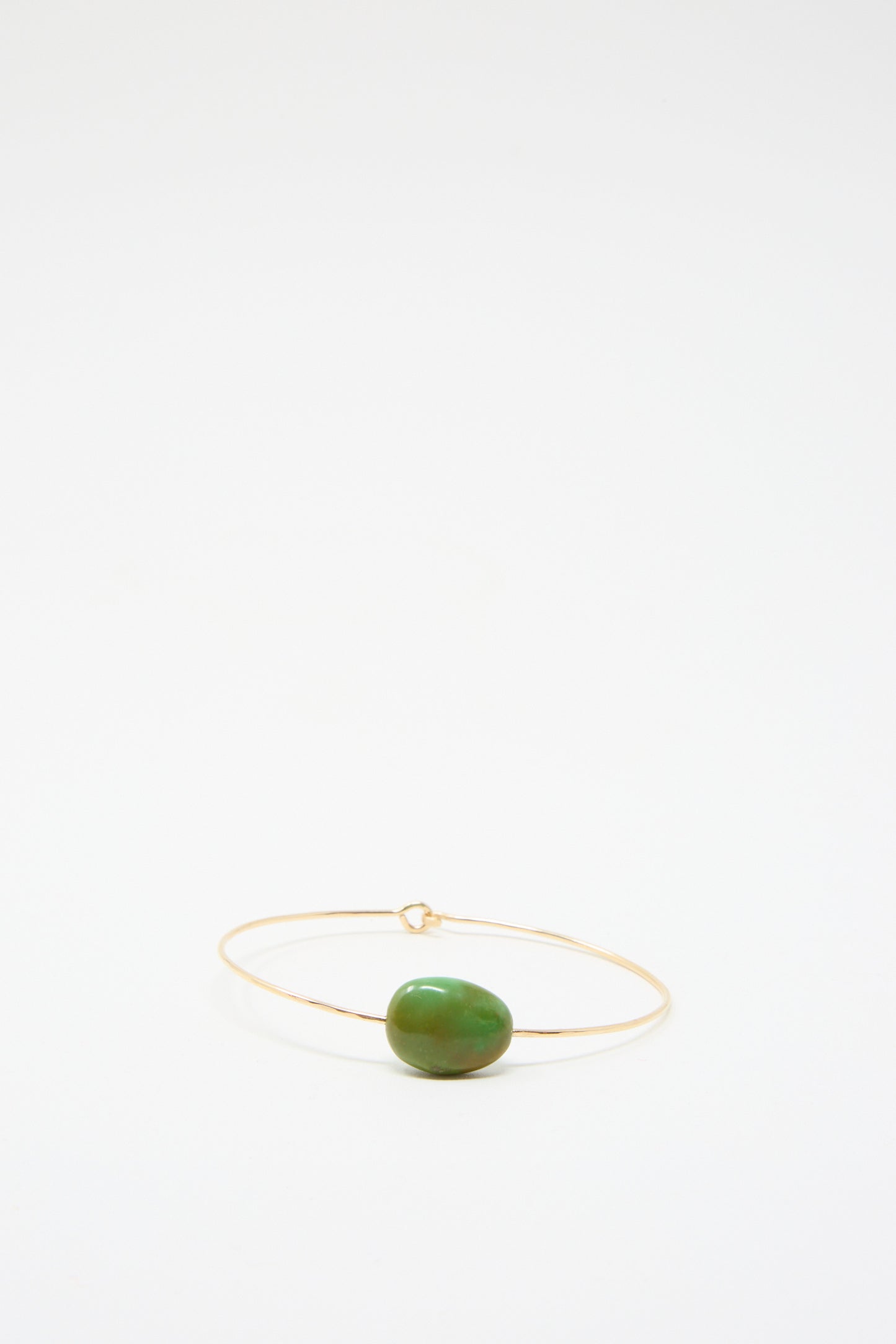 The "Stone Cuff in Turquoise" by Mary MacGill is a minimalist gold-filled bracelet showcasing a solitary turquoise stone,  set against a plain white background.