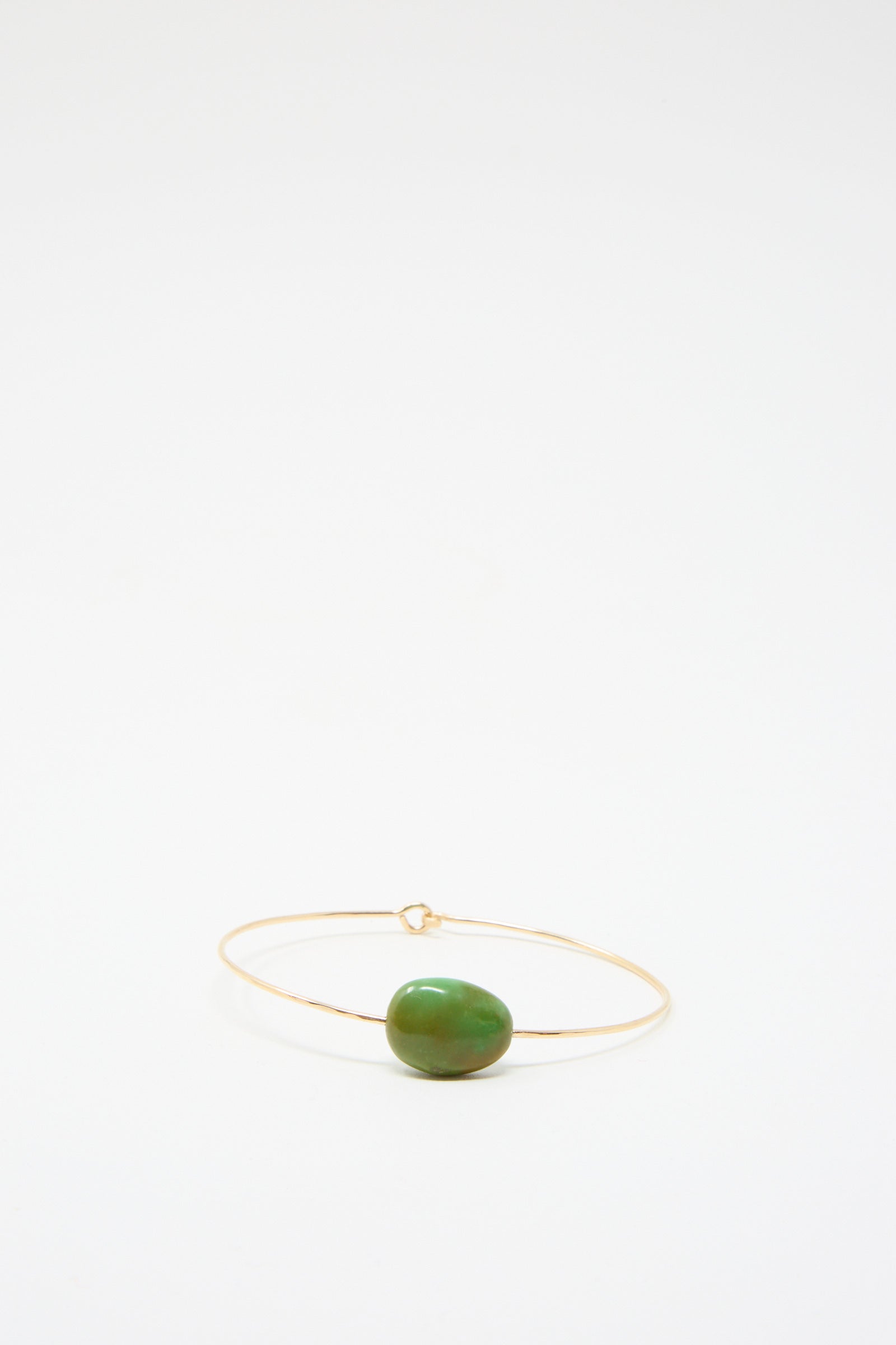 The "Stone Cuff in Turquoise" by Mary MacGill is a minimalist gold-filled bracelet showcasing a solitary turquoise stone,  set against a plain white background.