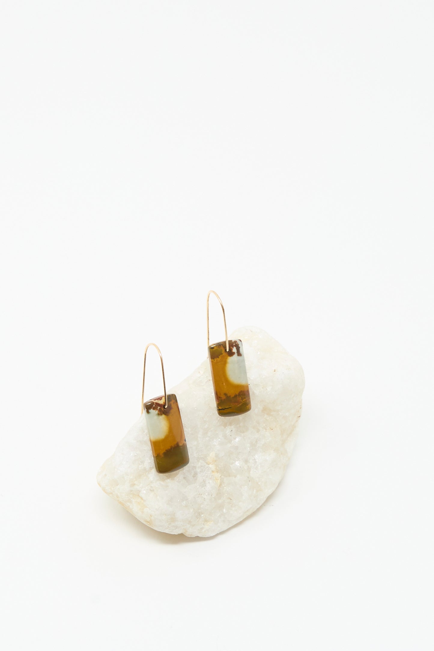 The Stone Drop Earrings in Blue Brown Agate Stone by Mary MacGill feature handmade rectangular agate dangles with 14k gold-filled accents, displayed on a white stone against a white background.