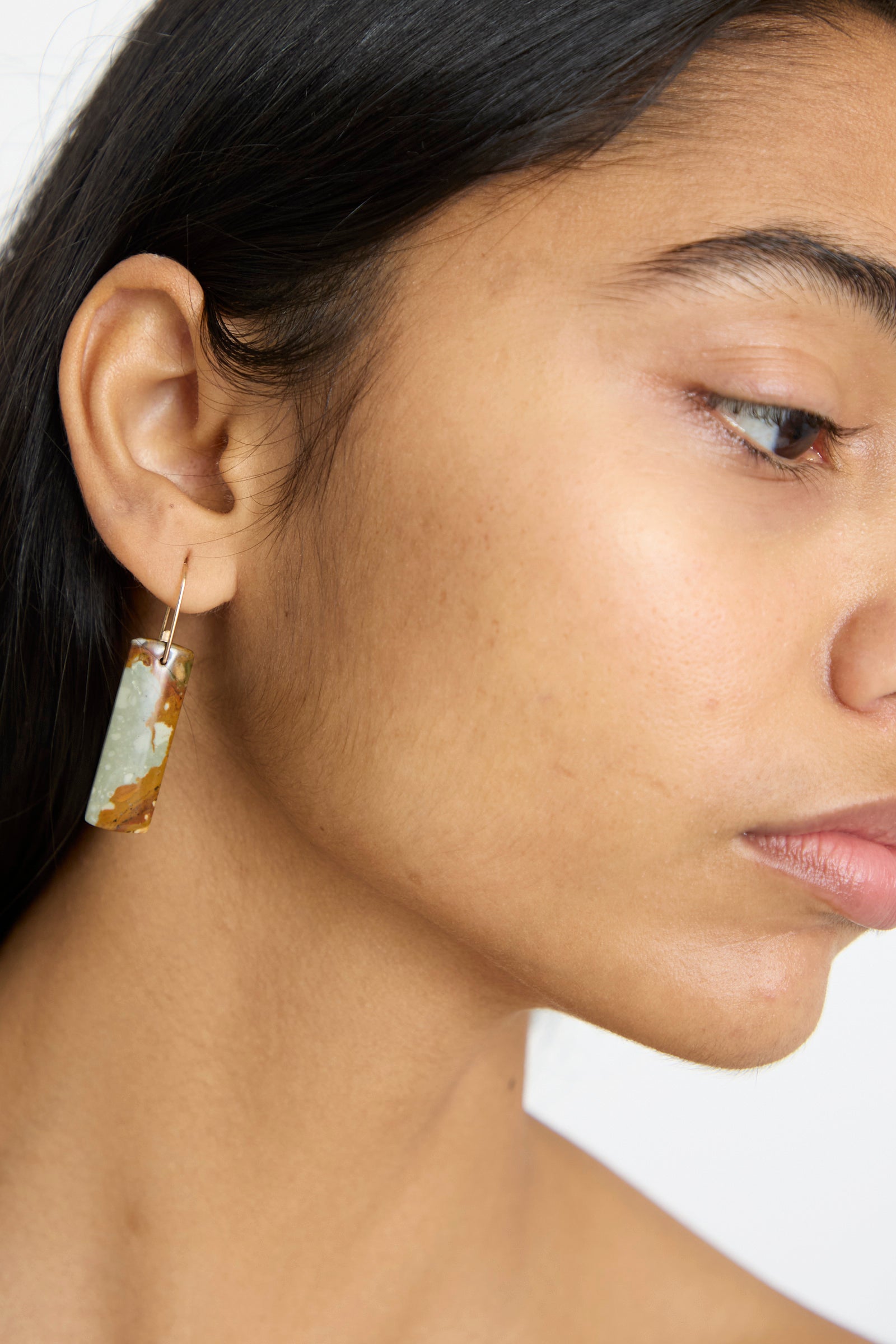 Close-up of a person wearing Mary MacGill's Stone Drop Earrings in Jasper, made with gold-filled wire and featuring a multicolored jasper stone.