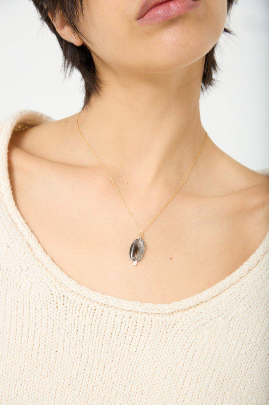 A woman wearing a white sweater and a Mary MacGill Stone Drop Necklace in Moss Aquamarine on a 14k gold-filled chain.