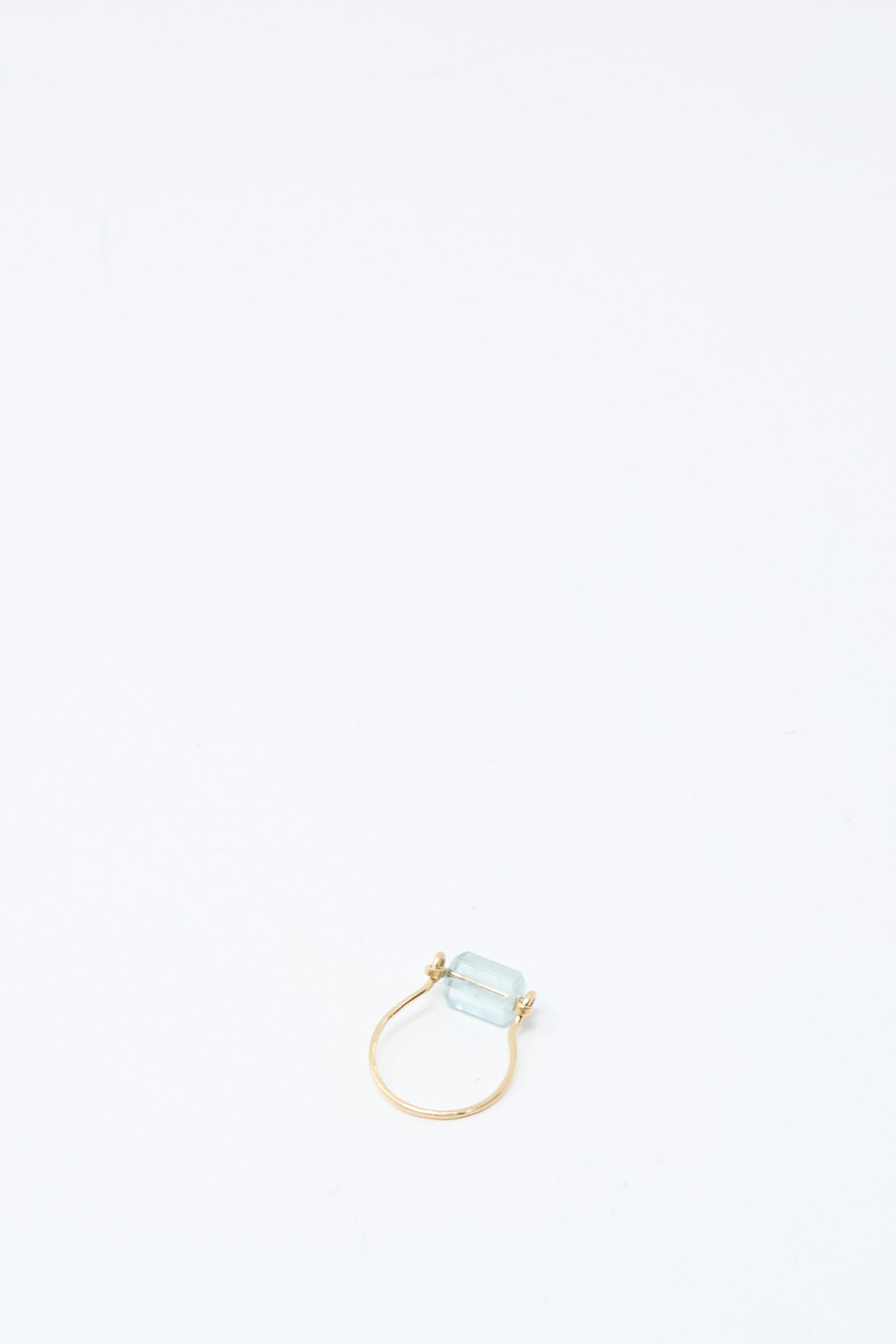 The Mary MacGill 14K Ring in Aquamarine Tube, featuring a handmade rectangular light blue gemstone, is positioned near the bottom center of a plain white background.