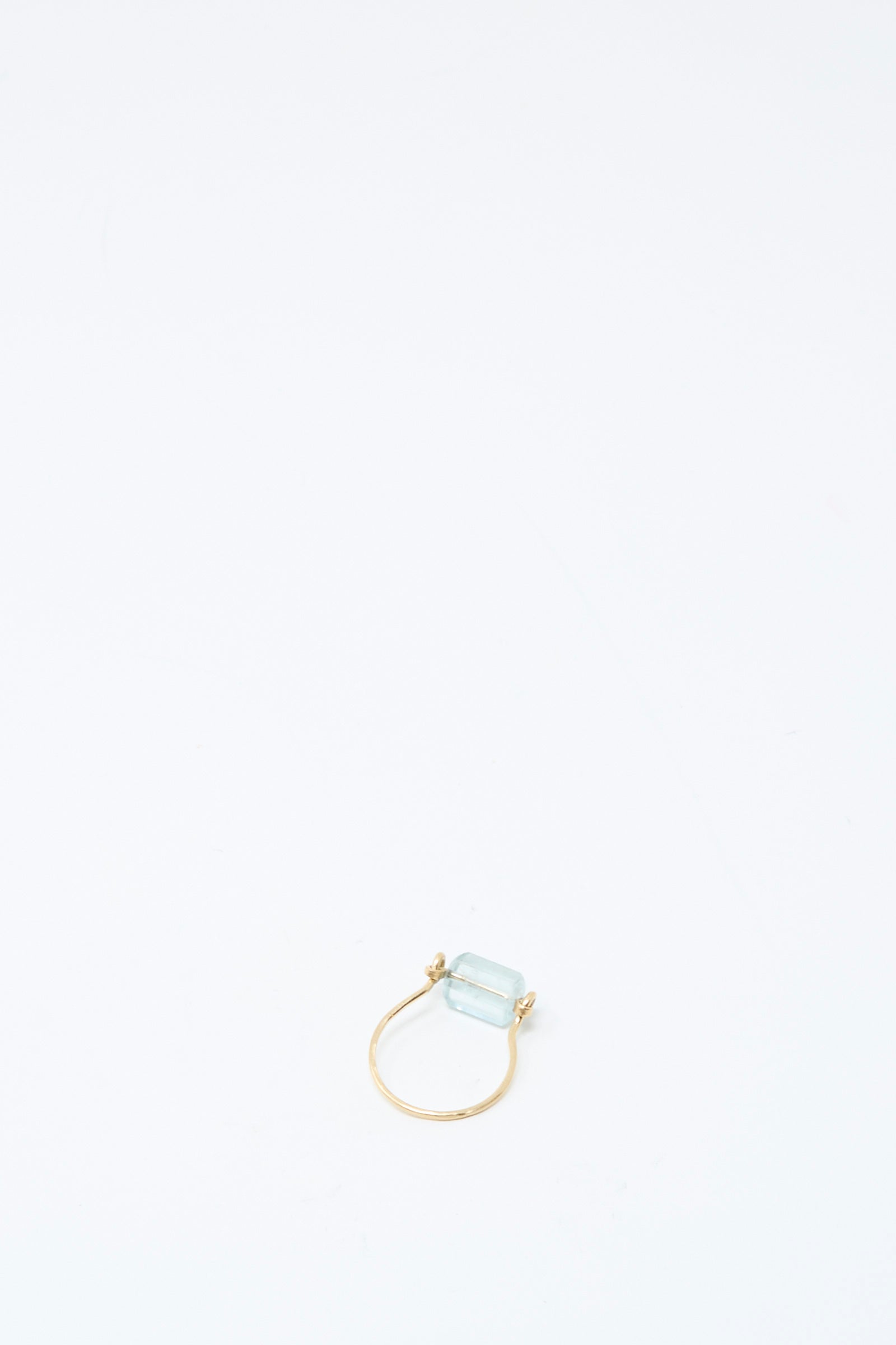 The Mary MacGill 14K Ring in Aquamarine Tube, featuring a handmade rectangular light blue gemstone, is positioned near the bottom center of a plain white background.