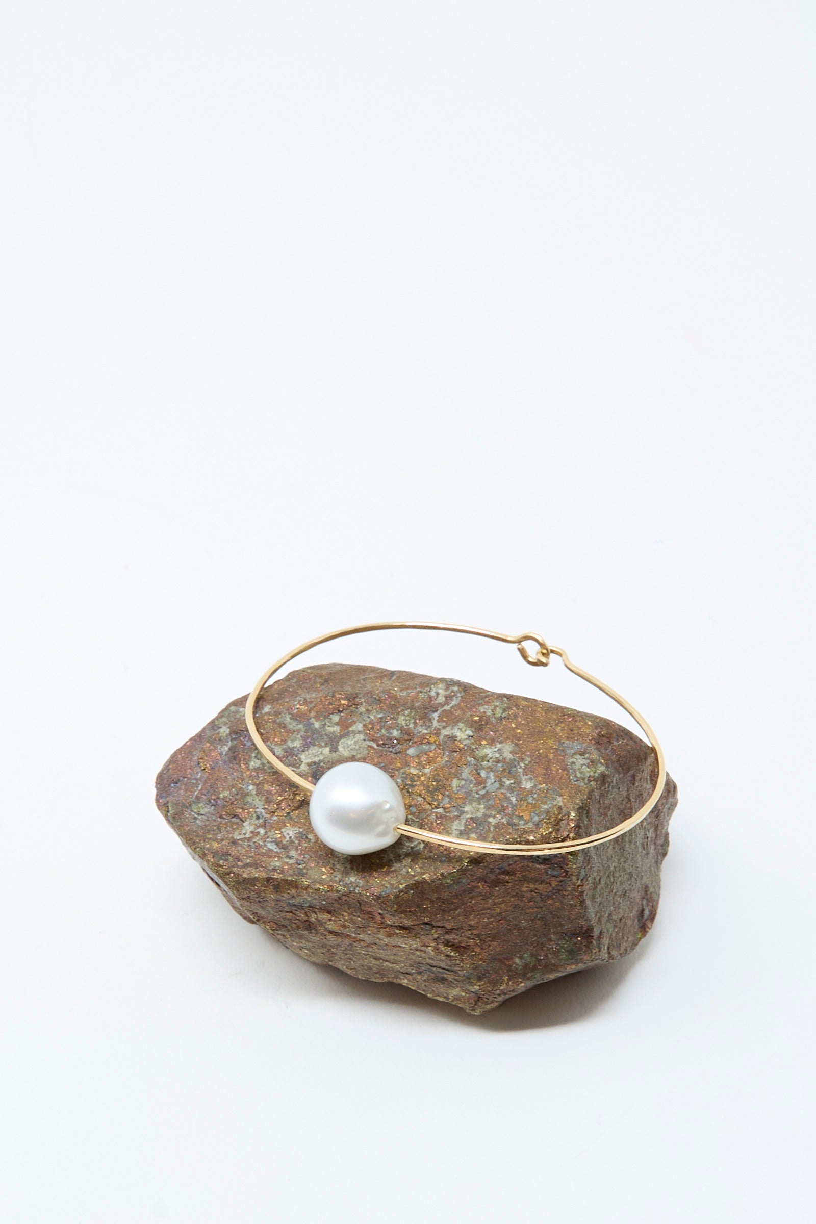 The Mary MacGill 14K Tahitian Pearl Cuff in White is shown resting on a rough brown rock with a plain white background, emphasizing the refined beauty of this handmade jewelry piece.