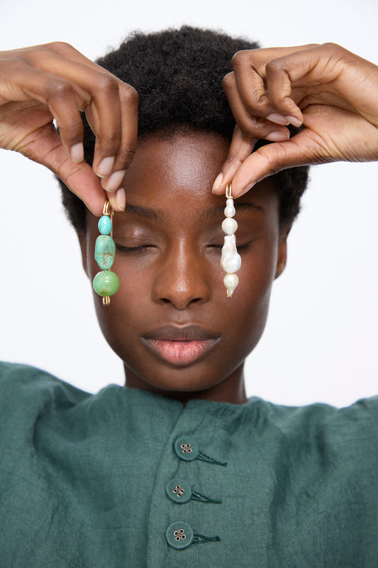 A person with eyes closed holds up a Chrysoprase and Turquoise Pin alongside an Quatro Pearl pin