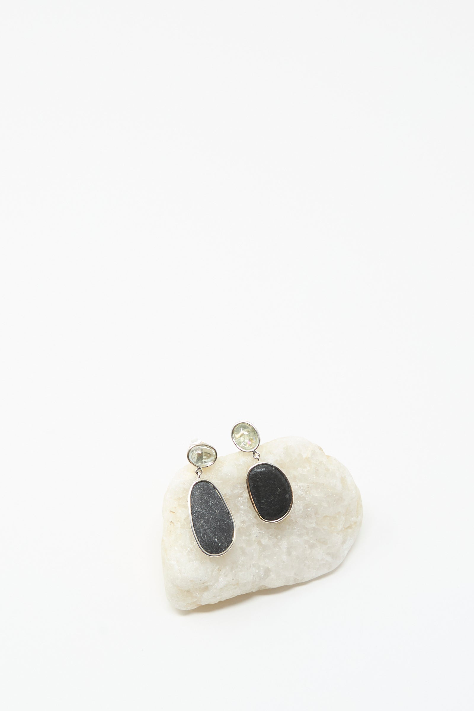 Mary MacGill Double Stone Drop Earrings in Dark Island Stone and Tourmaline are shown on a white stone against a plain white background, featuring black tourmaline ovals and clear round studs.