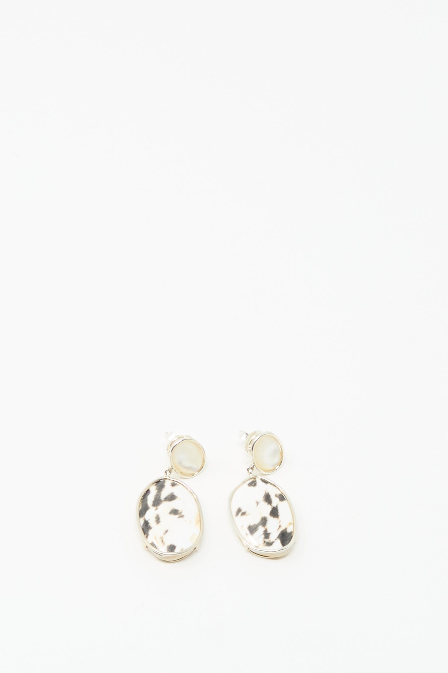 Mary MacGill's Double Stone Drop Earrings in Moonstone and Cowrie Shell feature gold-rimmed, oval pendants with black and white speckling, displayed on a white background.