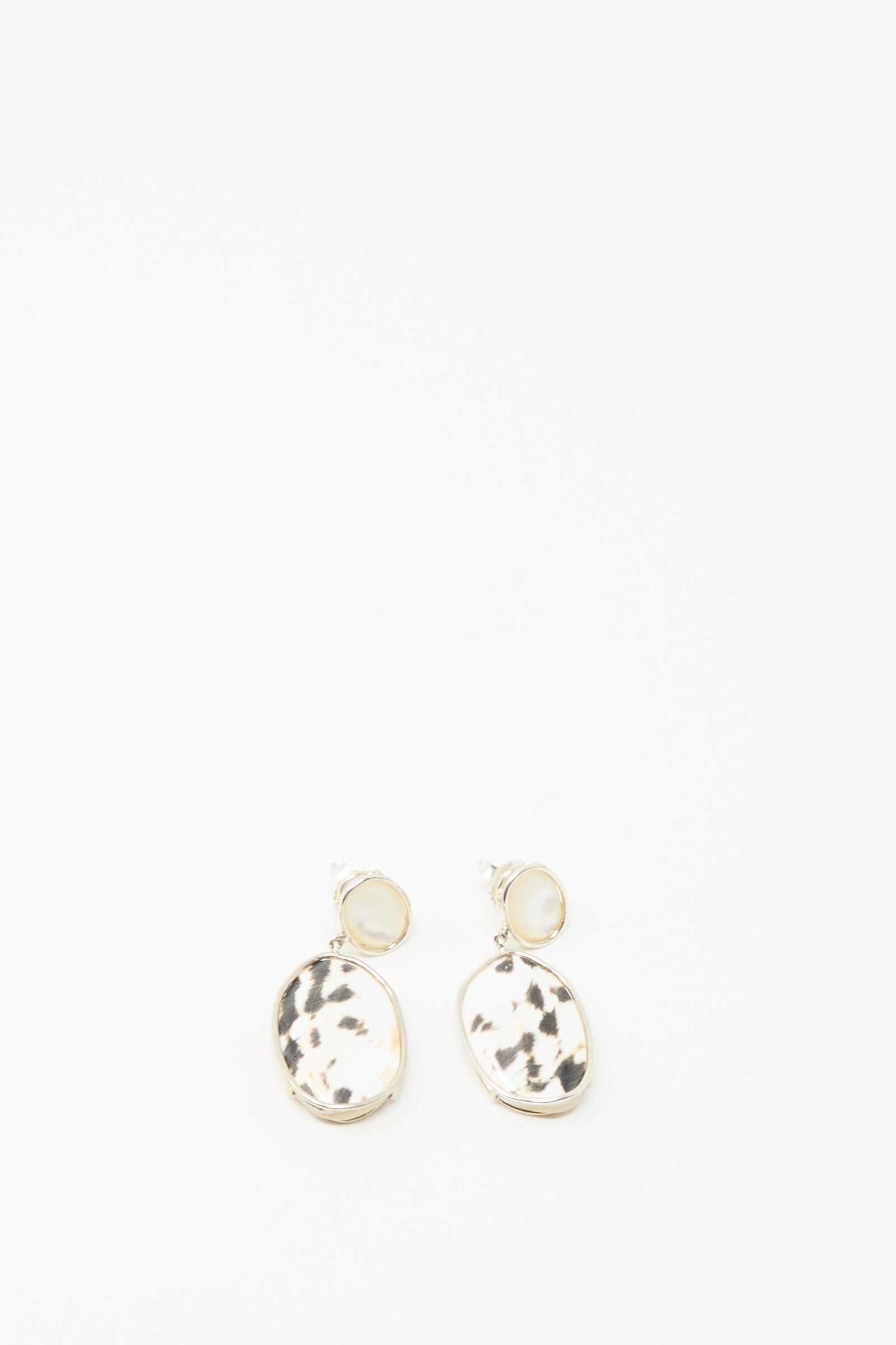 Mary MacGill's Double Stone Drop Earrings in Moonstone and Cowrie Shell feature gold-rimmed, oval pendants with black and white speckling, displayed on a white background.