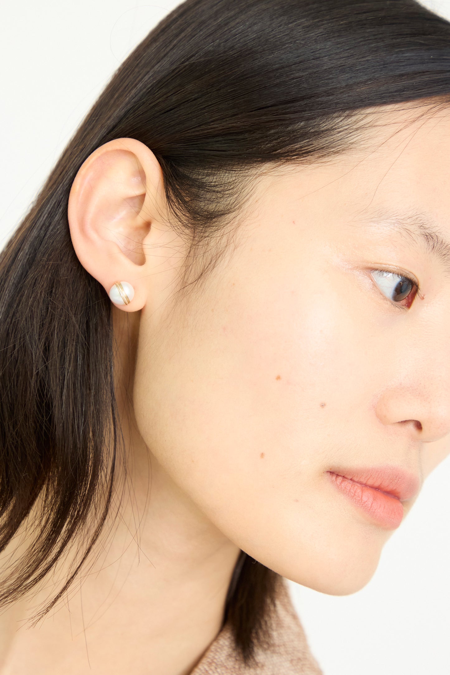 A close-up shows a person with straight black hair wearing Mary MacGill's Grand Baroque Pearl Studs in White.