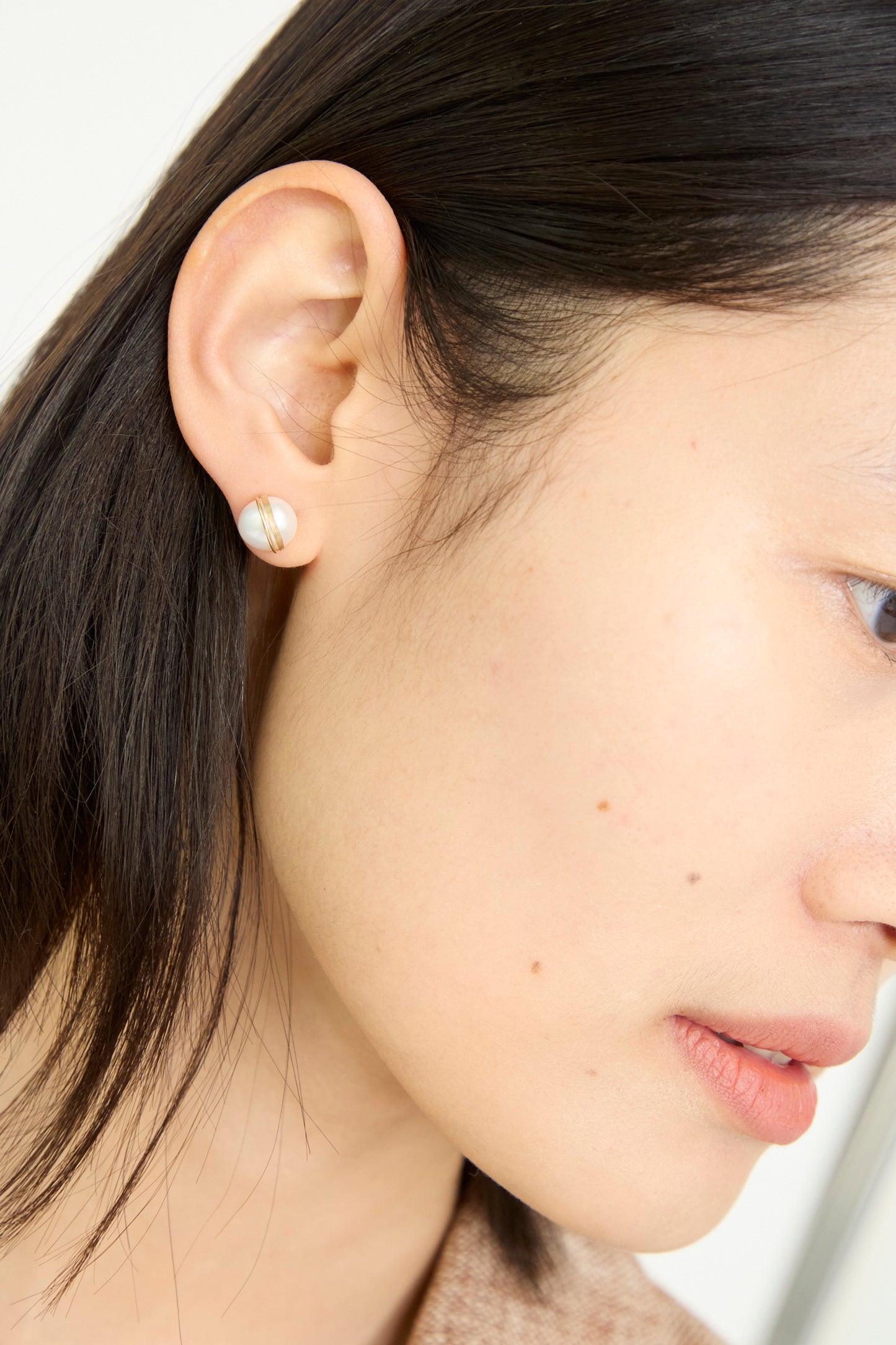 A close-up of a model's ear showcases the Grand Baroque Pearl Studs in White by Mary MacGill, against a white backdrop.