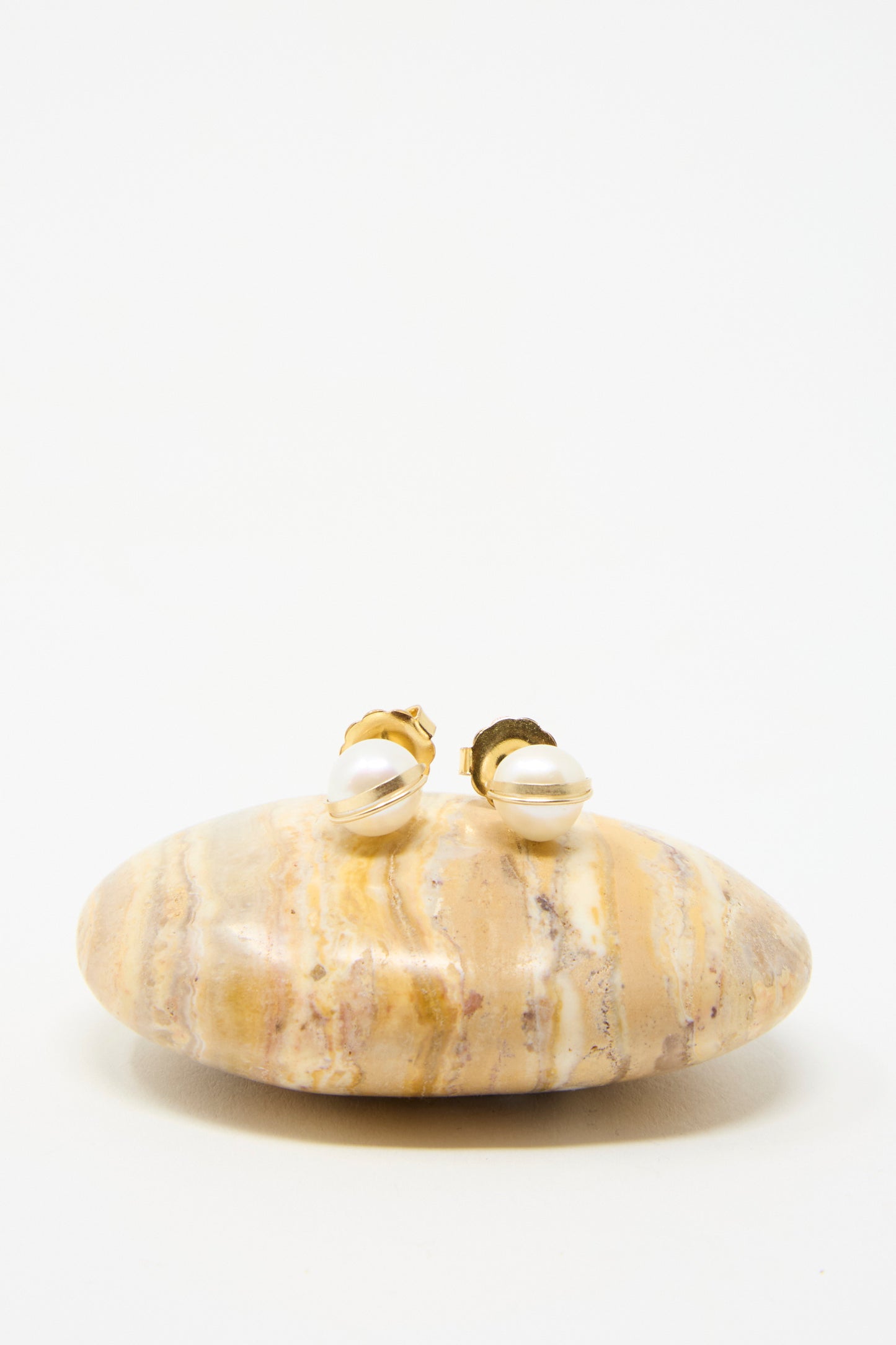 The Grand Baroque Pearl Studs in white by Mary MacGill are beautifully handcrafted with gold-filled details and highlighted by Baroque pearl accents, presented on a marble stone against a white background. 