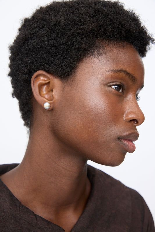 A person wearing a handmade Grande Baroque Pearl Studs in Silver earring, featuring a baroque pearl accented by a horizontal gold-filled wire band.