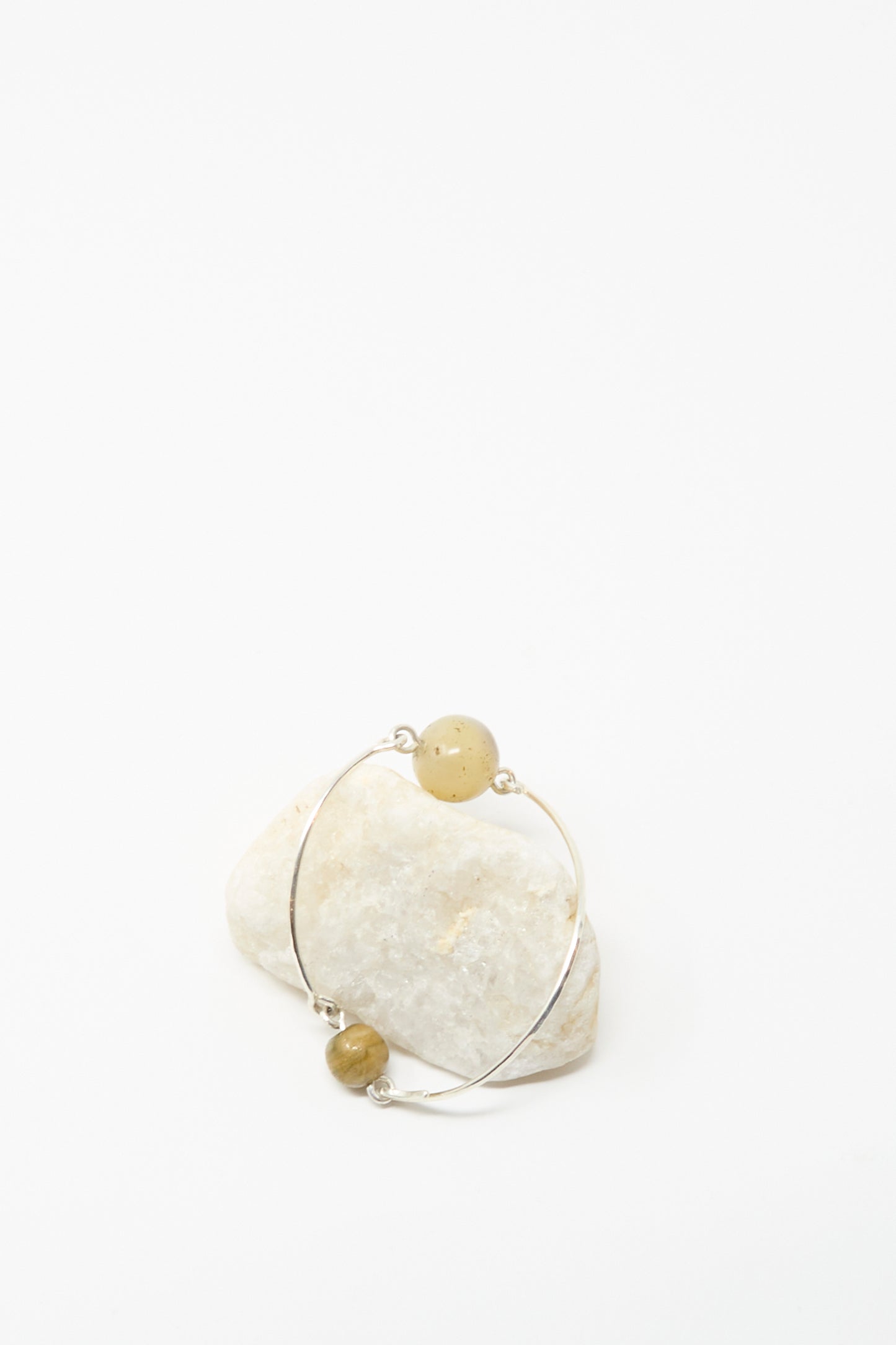 Mary MacGill's Hammered Sterling Silver Bangle with Ancient Agate Trade Beads features two round yellow stones and is shown leaning against a white stone on a plain white background.