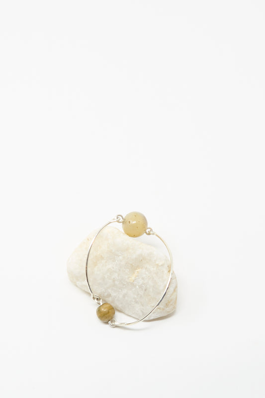 Mary MacGill's Hammered Sterling Silver Bangle with Ancient Agate Trade Beads features two round yellow stones and is shown leaning against a white stone on a plain white background.