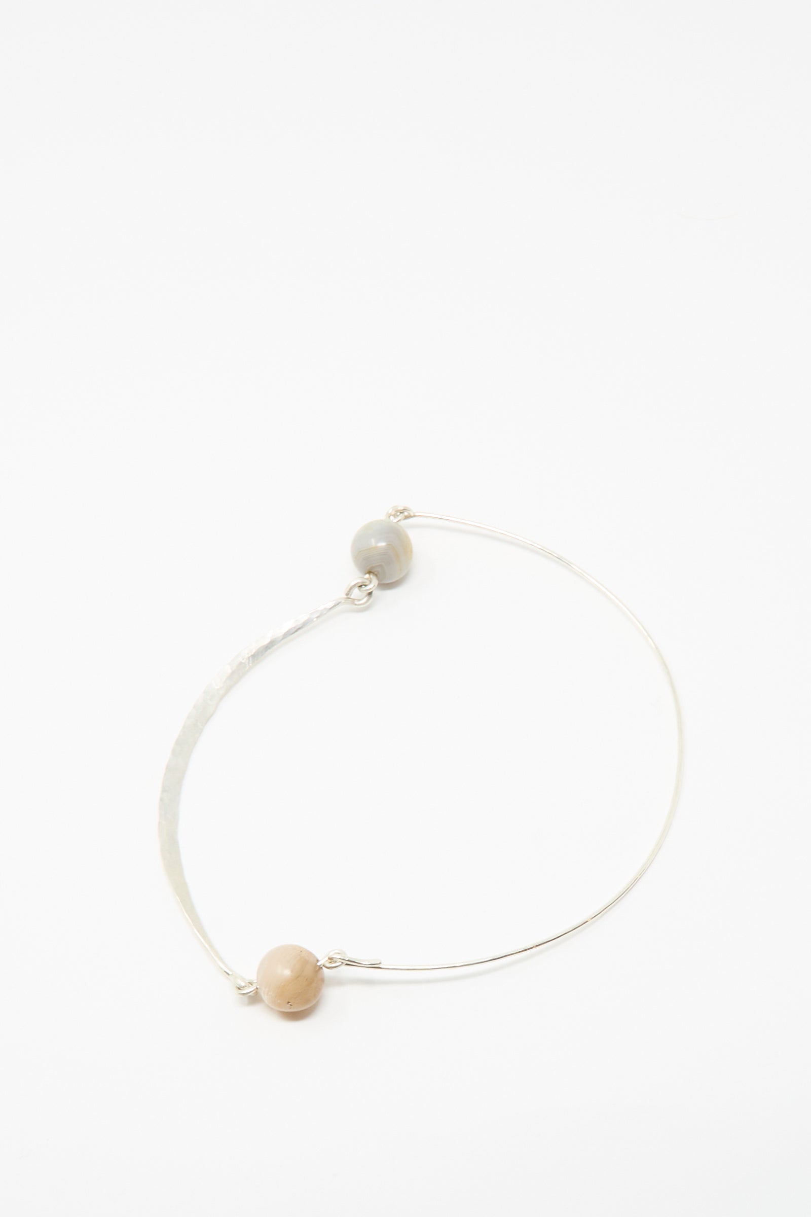 Mary MacGill’s Hammered Sterling Silver Collar features ancient agate trade beads—one beige, one gray—set apart on the curved band, showcasing handmade artistry against a white background.