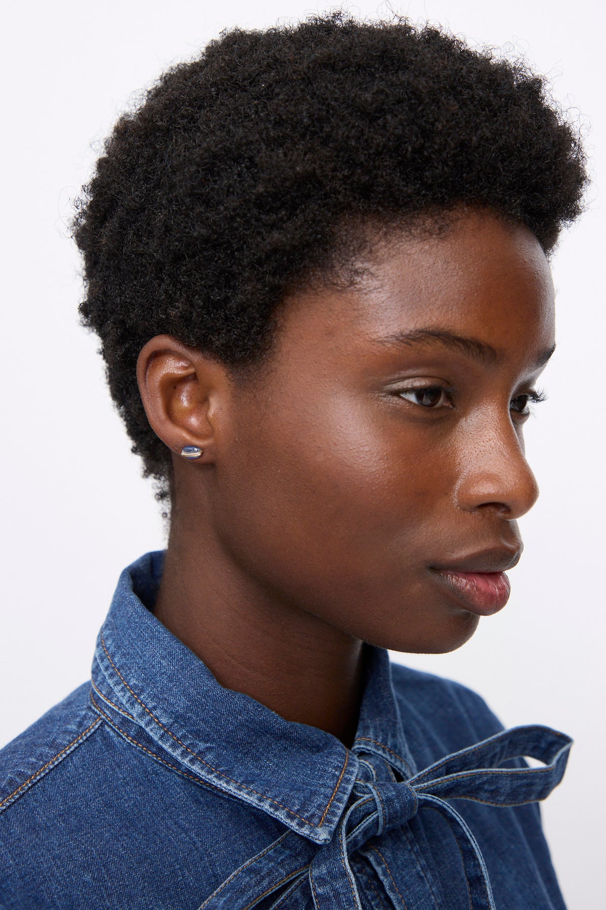 Profile view of a person wearing a Mary MacGill Kyanite Stud, an oval-shaped stone set in gold-filled wire.