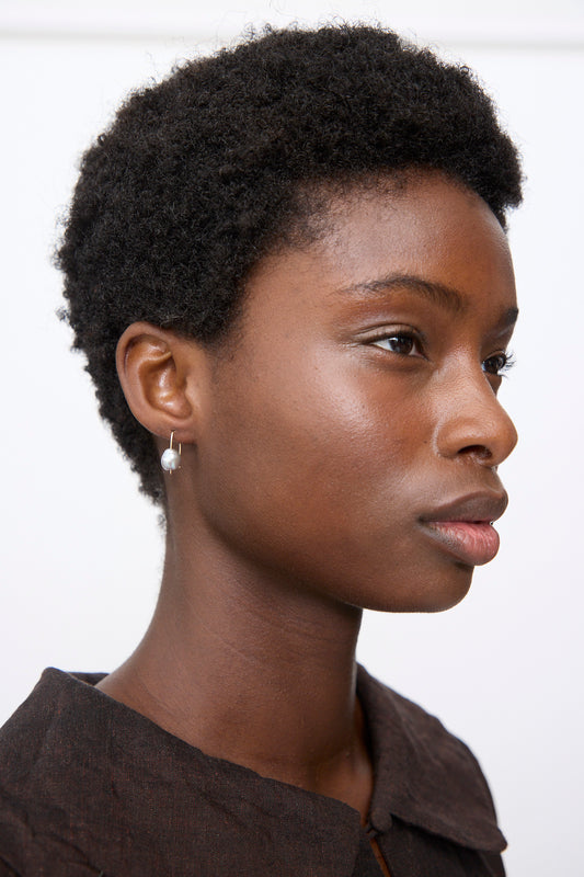 Profile view of a person wearing a small, silver Petite Baroque Pearl Drop Earrings on a gold-filled wire hook.