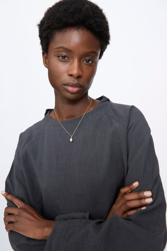 A person wearing a Petite Baroque Pearl Drop Necklace by Mary MacGill featuring a small baroque pearl pendant on a gold filled chain.