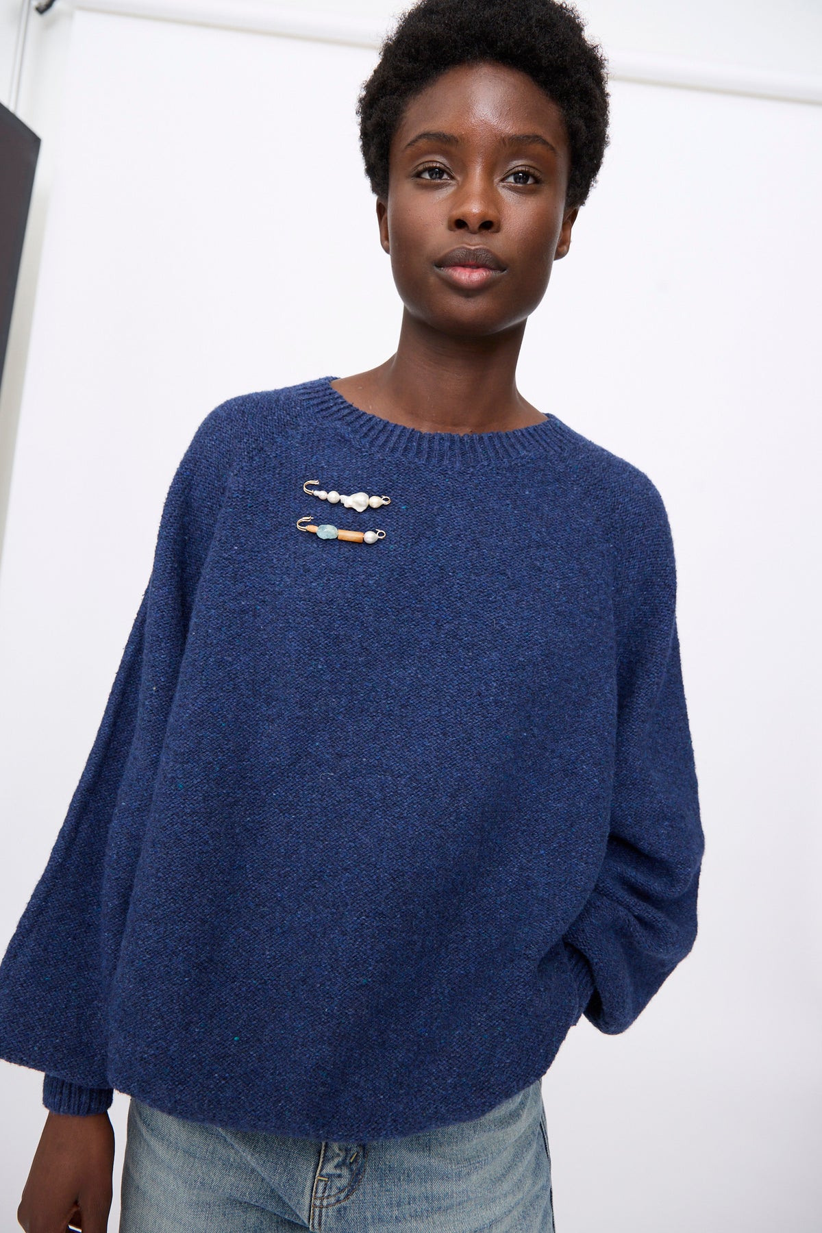 A person wearing a blue sweater pinned with the Mary MacGill Quatro Pearl Pin featuring baroque pearls and gold-filled wire.
