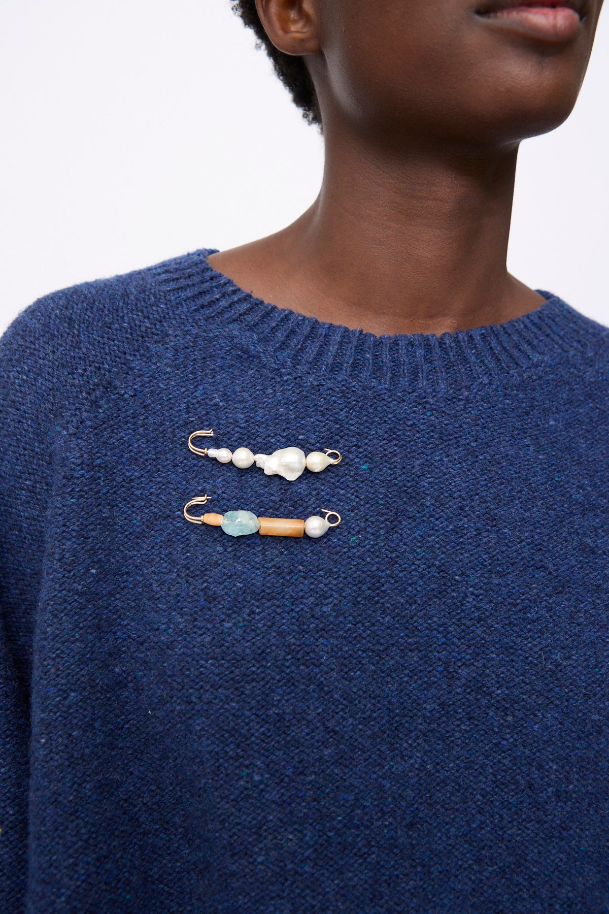 Two gold-filled pins worn on a blue knit sweater; the top pin features baroque pearls, and the bottom pin features a blue stone and an orange bead.