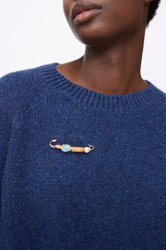 A Mary MacGill Rising Summer Pin featuring a gold baroque pearl and blue and orange stones, worn on a blue knit sweater.