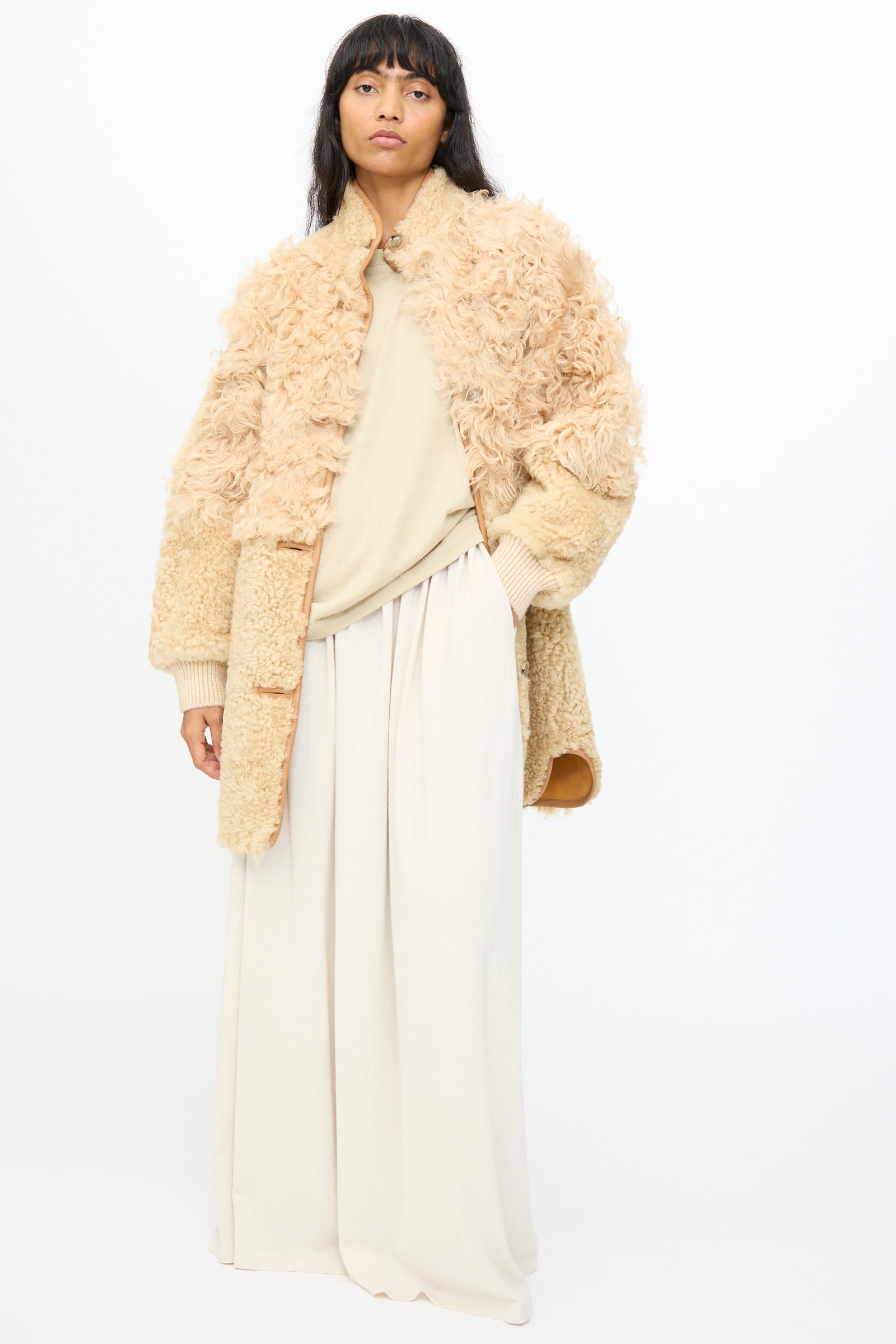 A person wearing the Milena Silvano Allie Coat in Oat, a light beige shirt, and wide-leg cream pants stands against a plain white background.
