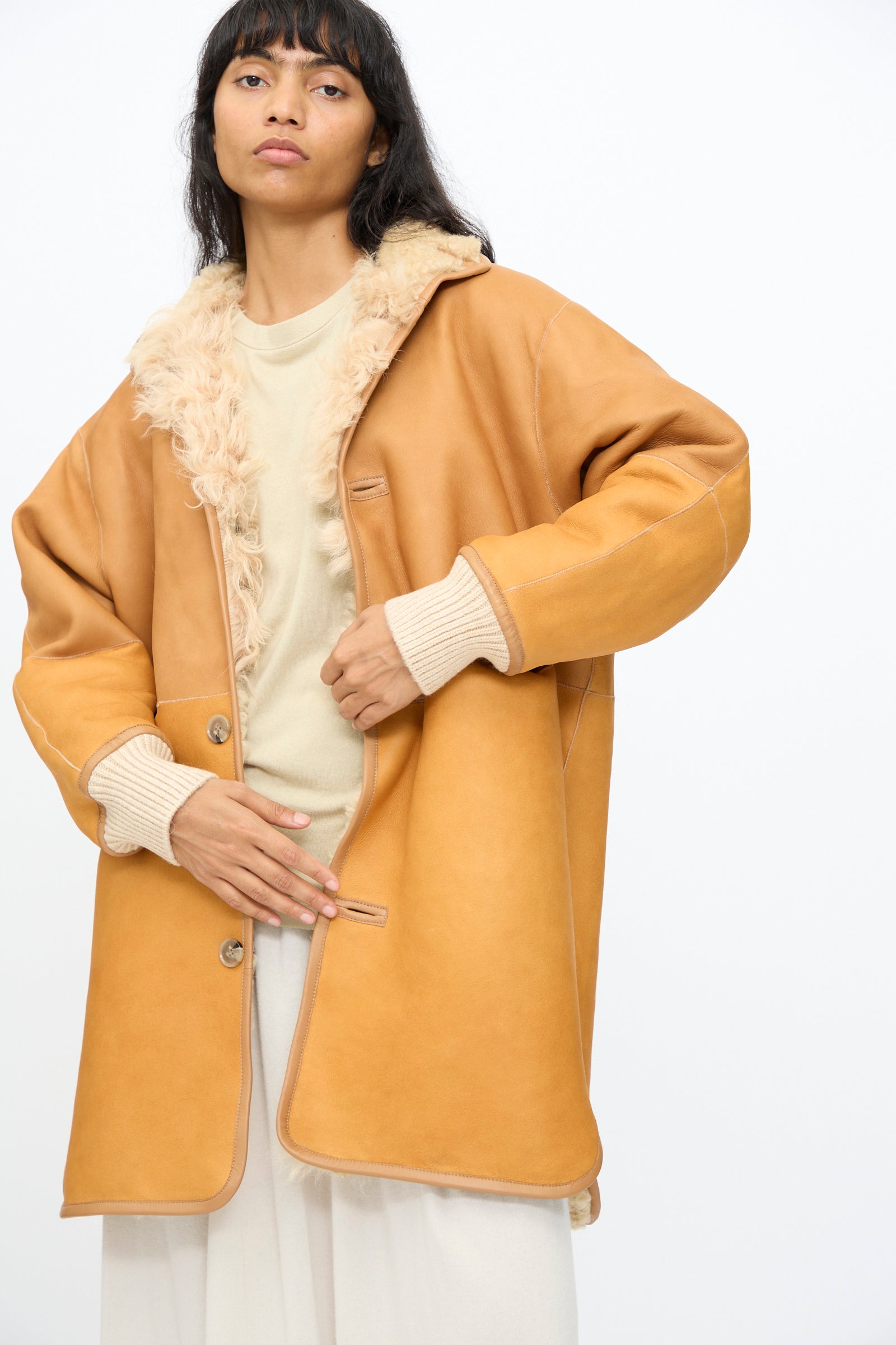 A woman wearing the Milena Silvano Allie Coat in Oat over a light sweater and white skirt stands against a plain white background.