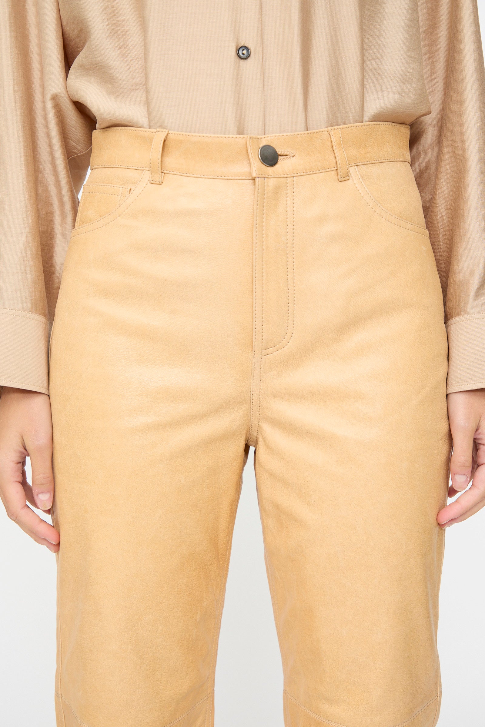 A person wearing a beige button-up shirt tucked into Milena Silvano Leather 5 Pocket Trousers in Bare—a high waist, straight fit pant crafted from vegetable tanned leather—with their hands resting by their sides.