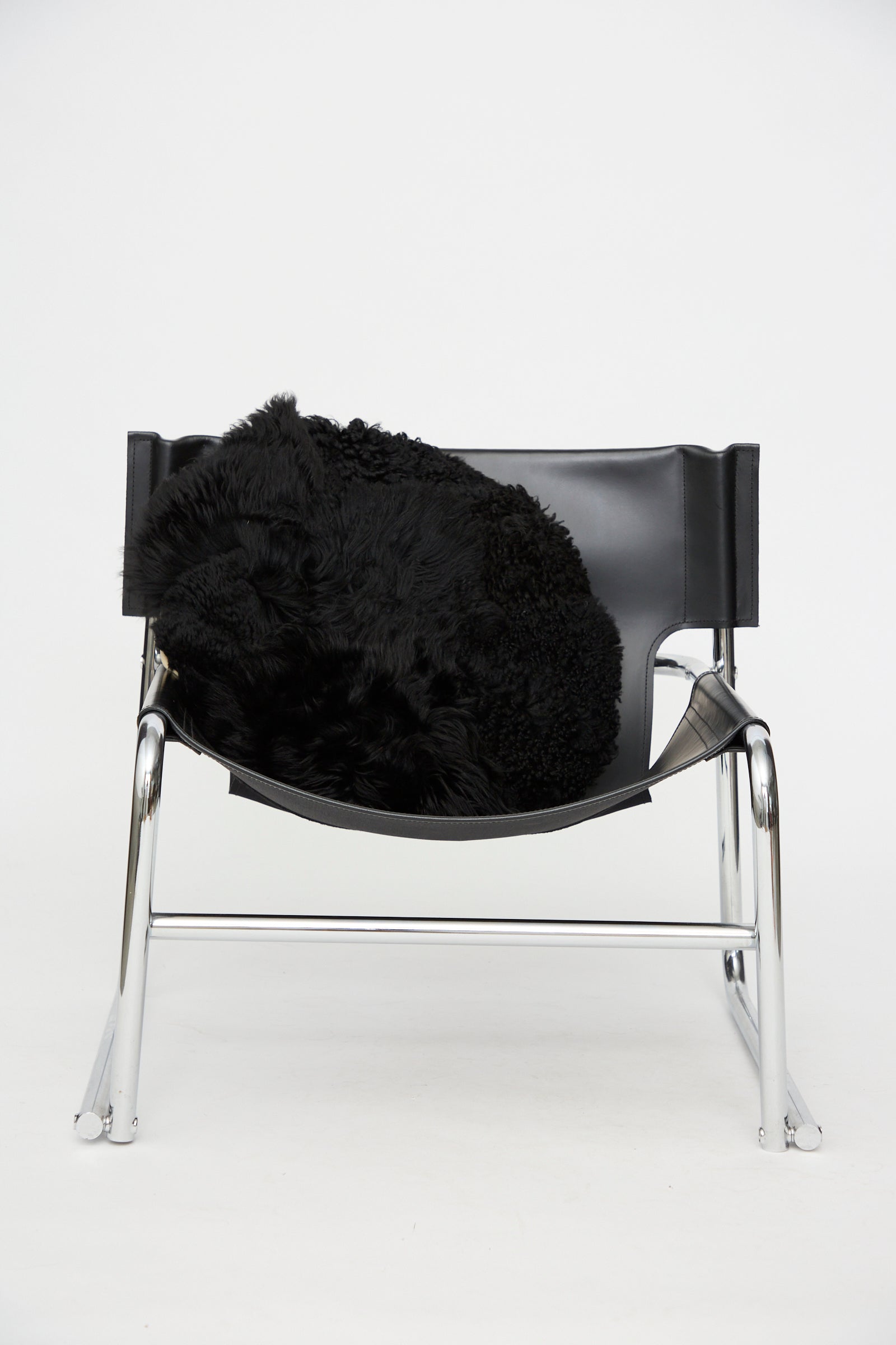 A modern black leather and chrome chair with a black fur throw draped over the seat is set against a plain white background, perfectly complemented by the Milena Silvano Shaggy Sheepskin Large Floor Pillow in Black for added comfort and style.