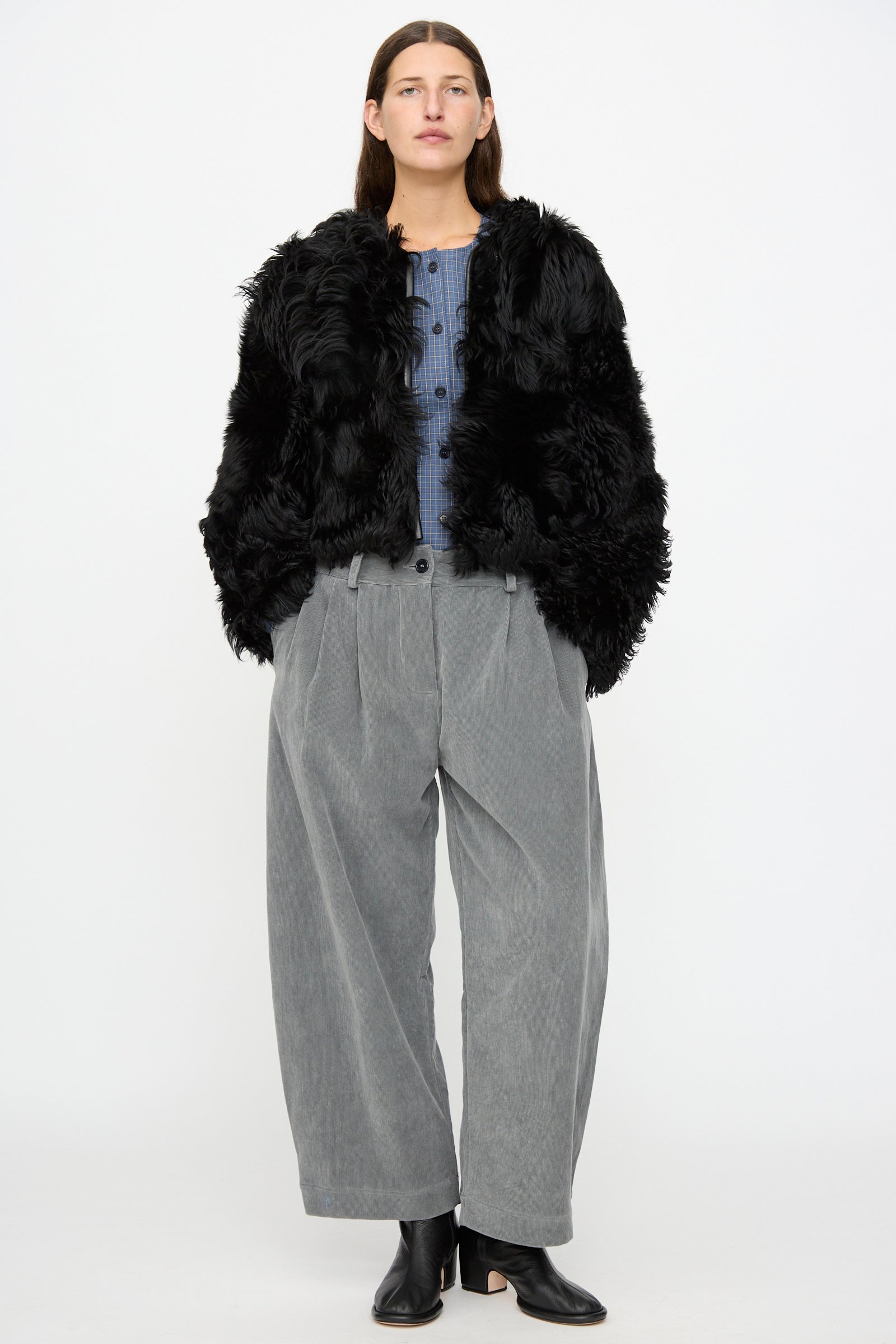 A person stands facing forward against a plain white background, wearing the Milena Silvano Shaggy Sheepskin Rainer Jacket in Black.