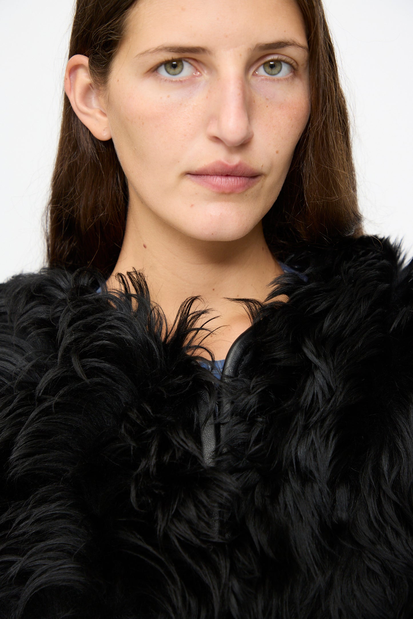 A woman with straight brown hair, wearing the limited edition Milena Silvano Shaggy Sheepskin Rainer Jacket in Black, looks at the camera against a plain white background.