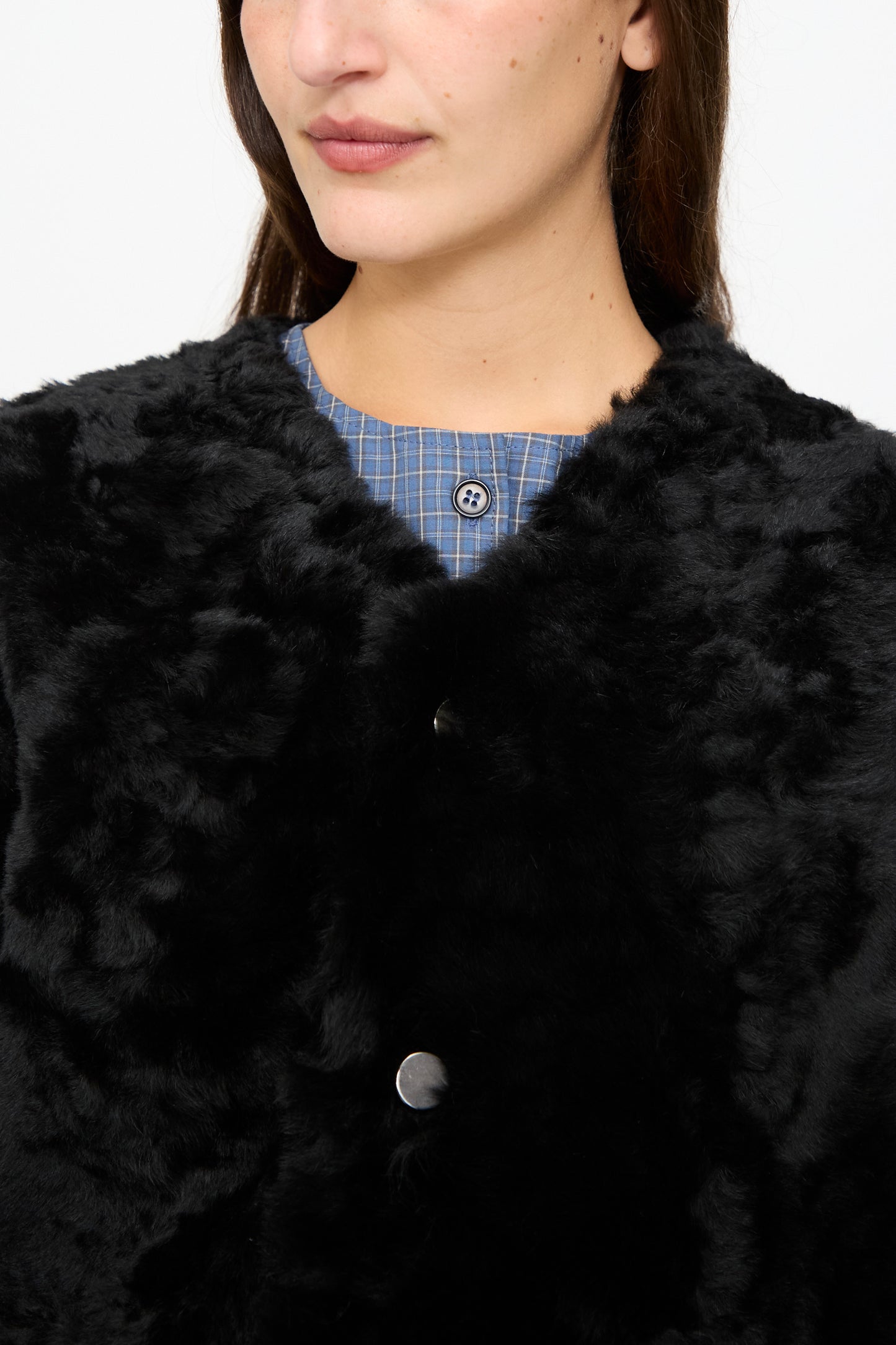 A woman wearing the Milena Silvano Sheepskin Reversible Liner in Black, featuring a black faux fur exterior, layered over a blue plaid shirt with visible buttons; shown from shoulders to nose.