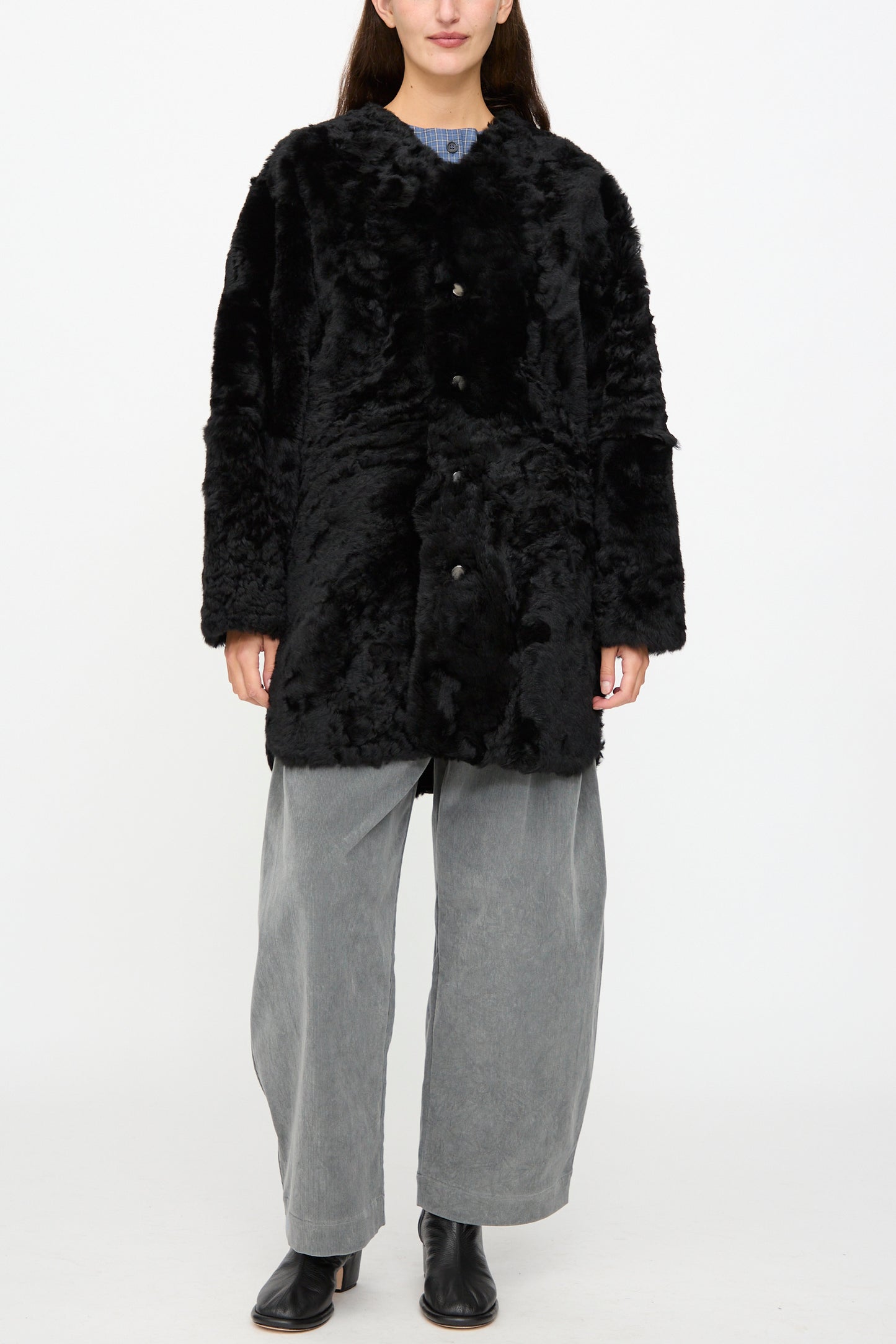 A person wearing the Milena Silvano Sheepskin Reversible Liner in Black, paired with gray wide-leg pants and black shoes, stands against a plain white background.