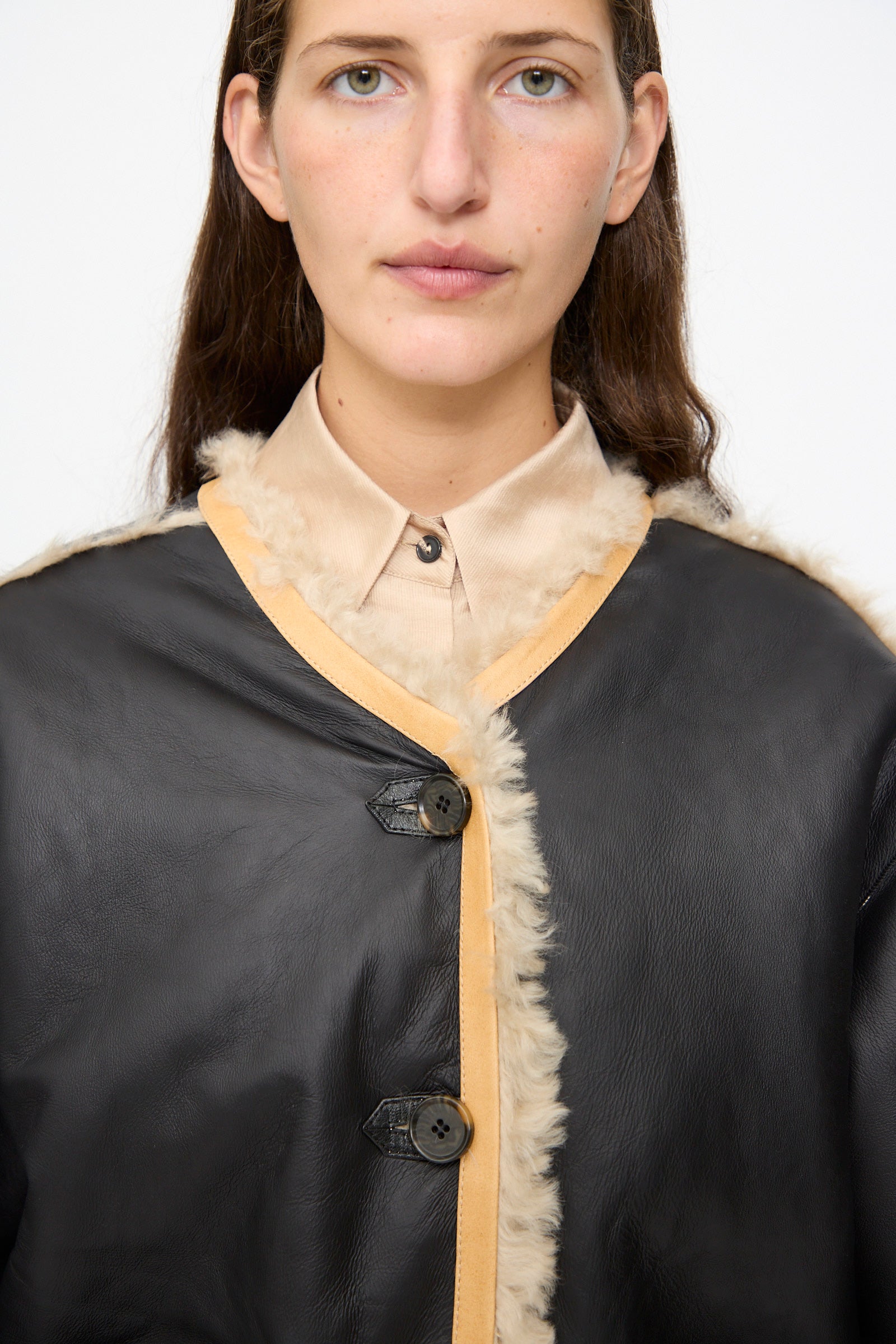 A person wearing the Milena Silvano Sheepskin Reversible Liner in Oat over a beige collared shirt, standing against a plain white background.